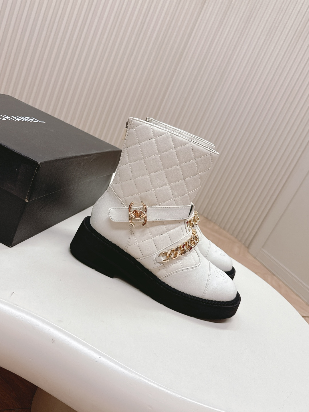 Luxury white quilted ankle boots with gold chain accents and a chunky black platform sole shown next to a designer box - Hình 2