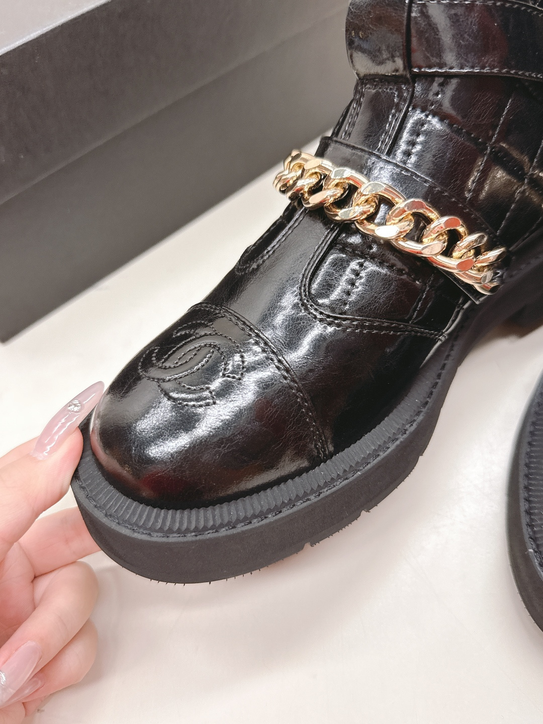 Black quilted leather ankle boots with gold chain strap and chunky rubber soles on a white surface. - Hình 7