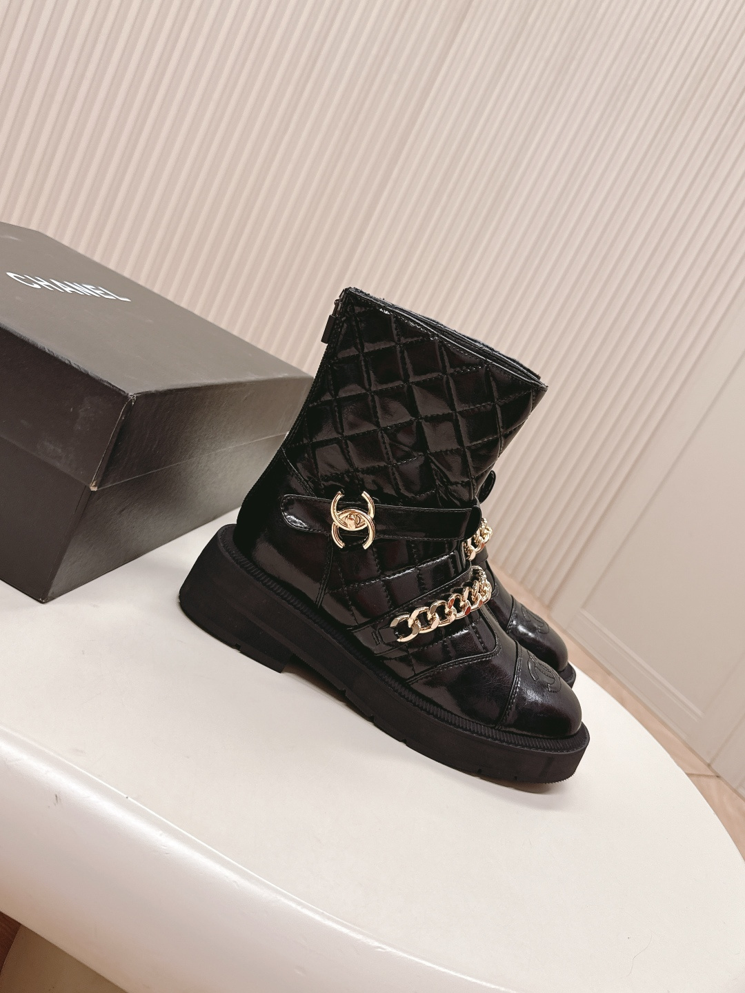 Black quilted leather ankle boots with gold chain strap and chunky rubber soles on a white surface. - Hình 6