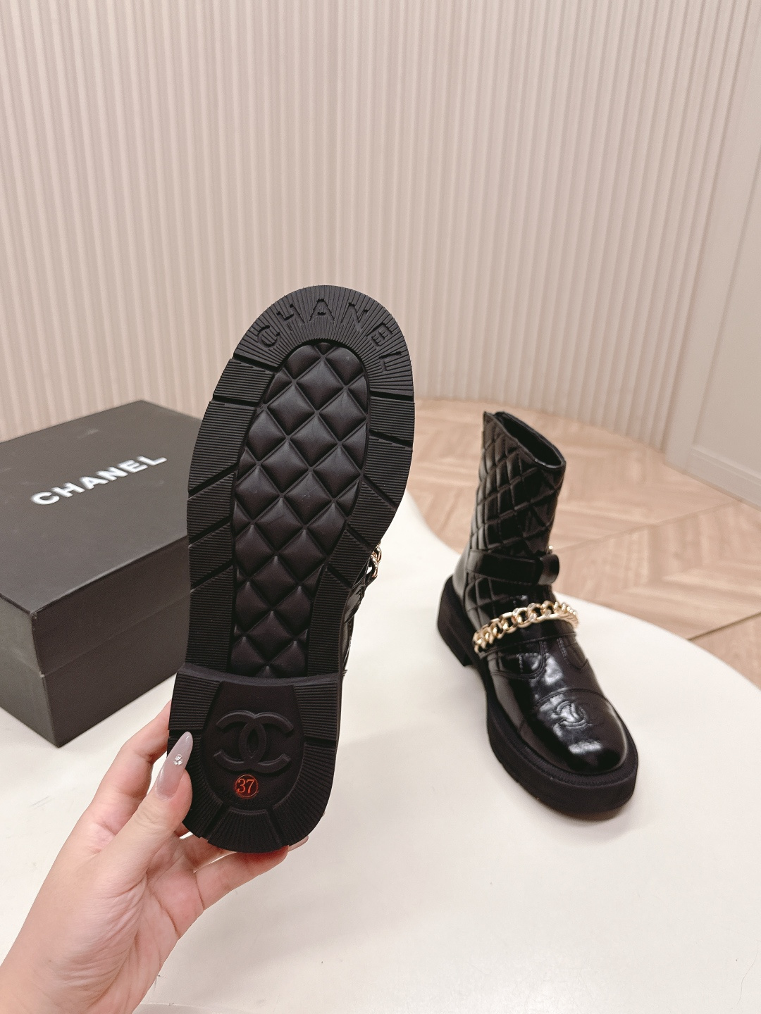 Black quilted leather ankle boots with gold chain strap and chunky rubber soles on a white surface. - Hình 4