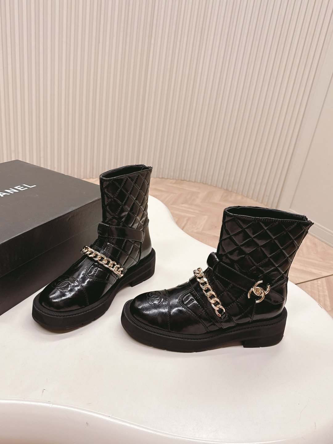 Black quilted leather ankle boots with gold chain strap and chunky rubber soles on a white surface. - Hình 2