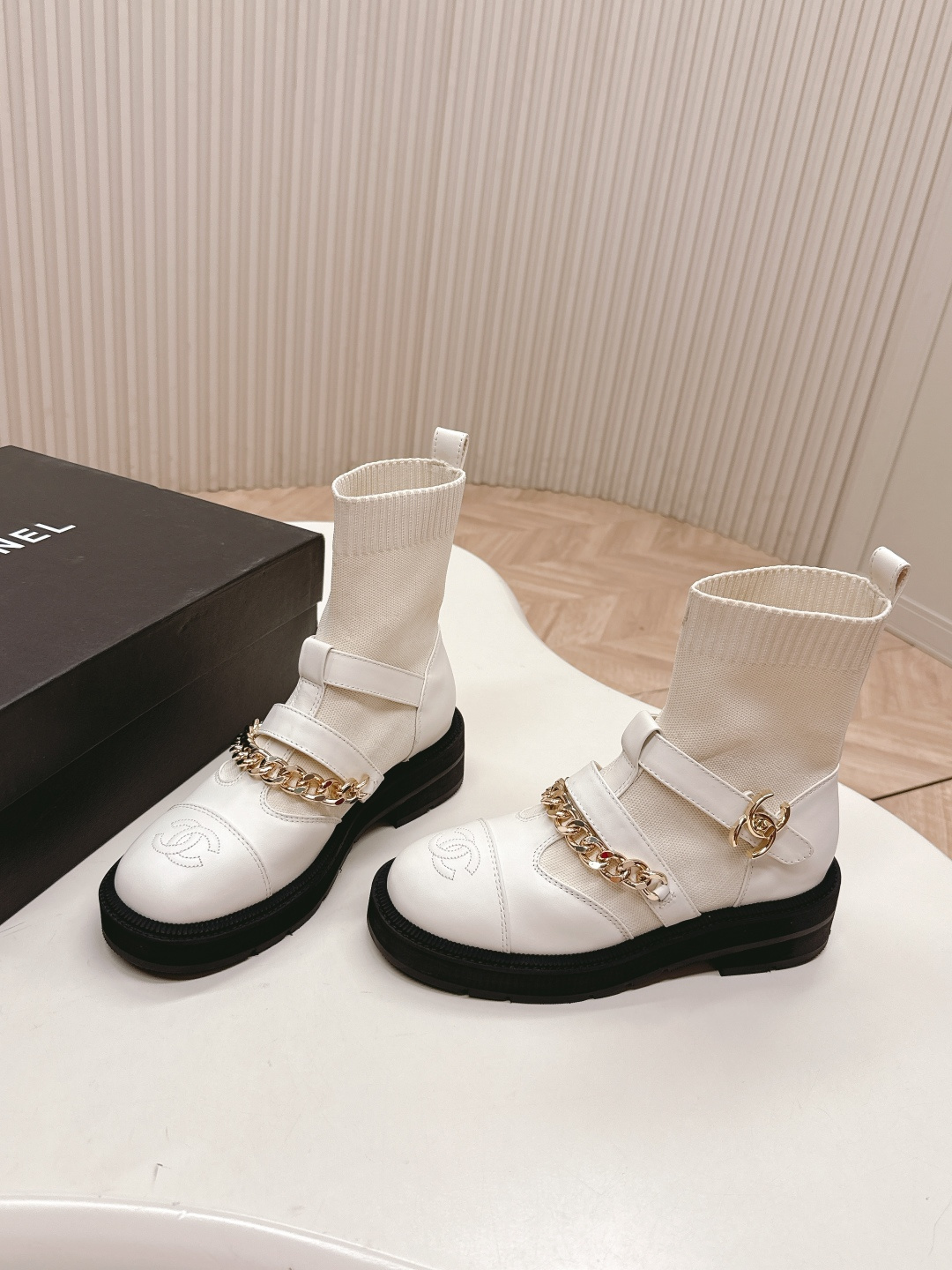 Pair of Chanel white leather sock ankle boots with gold chain and CC logo on a white table - Hình 2