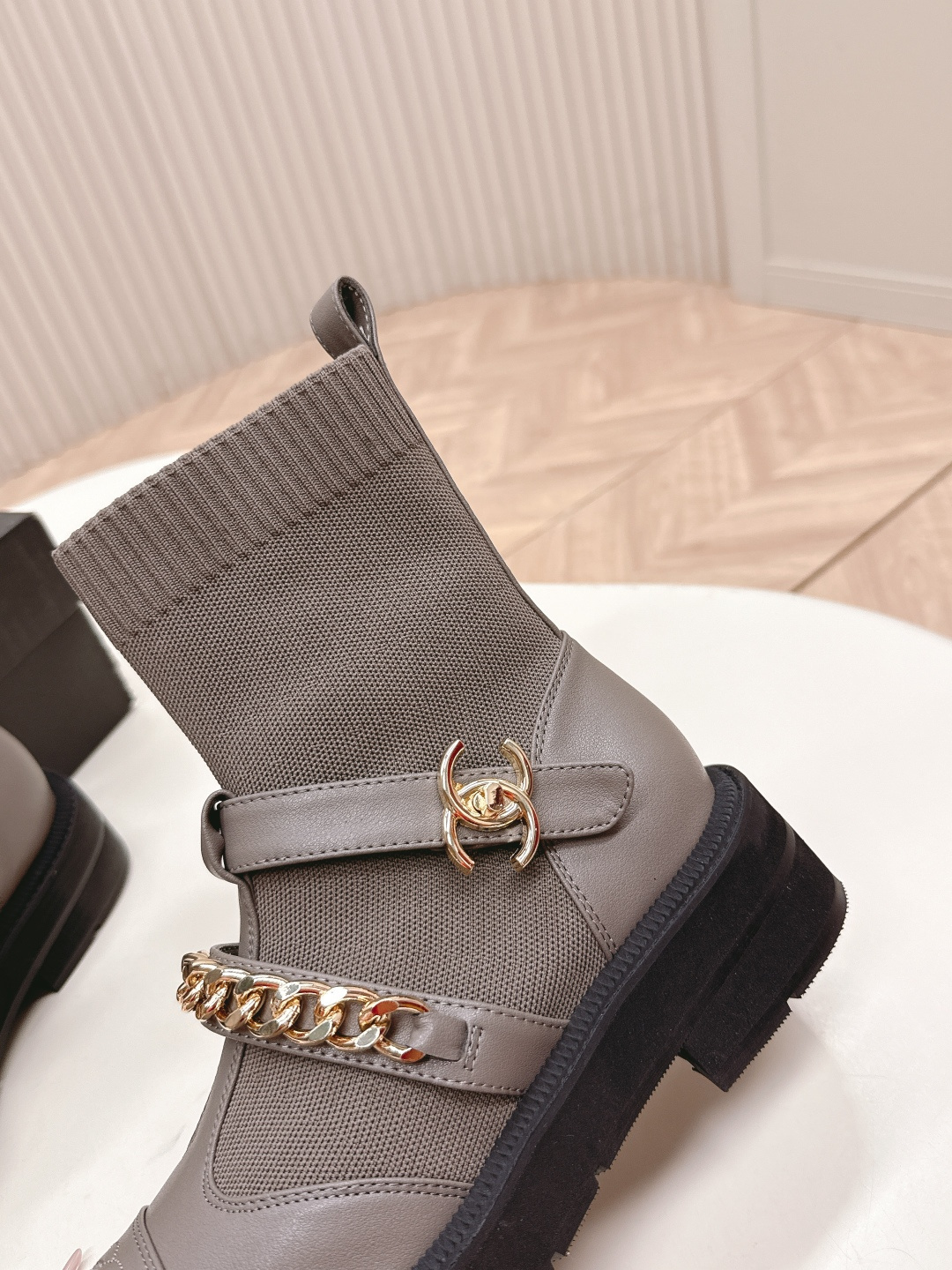 Pair of grey Chanel sock boots with gold chain details and CC logo on a white table near a Chanel box. - Hình 6