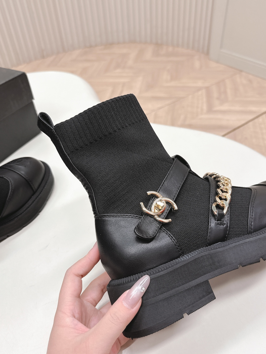 A pair of stylish black sock boots featuring gold chain hardware and chunky soles displayed on a white surface. - Hình 9