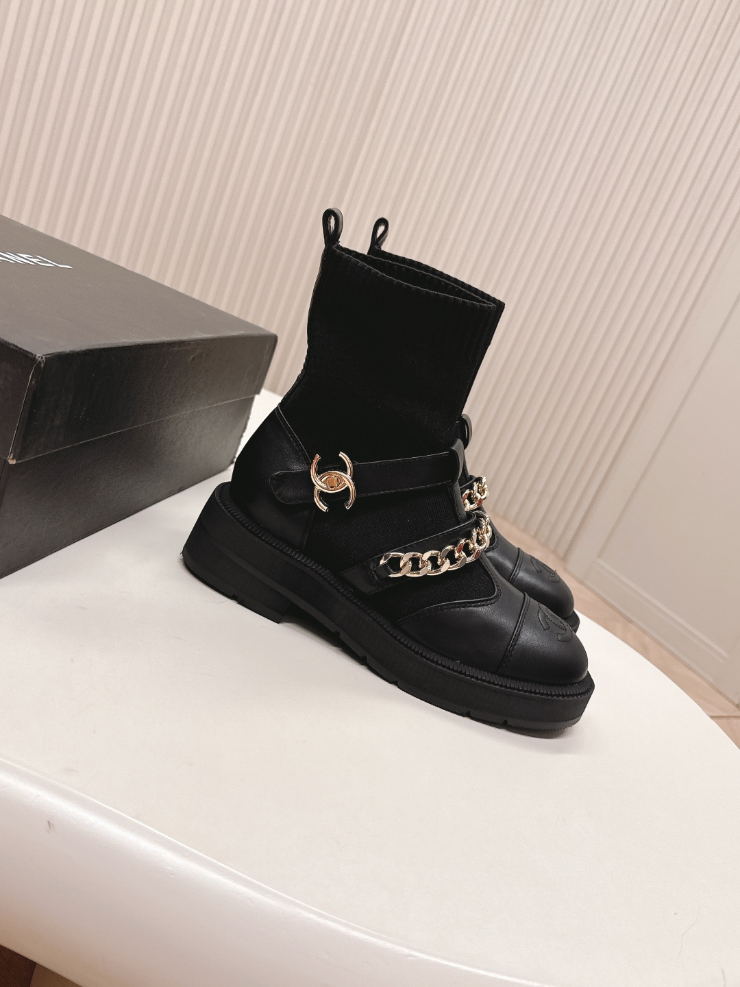 A pair of stylish black sock boots featuring gold chain hardware and chunky soles displayed on a white surface. - Hình 2