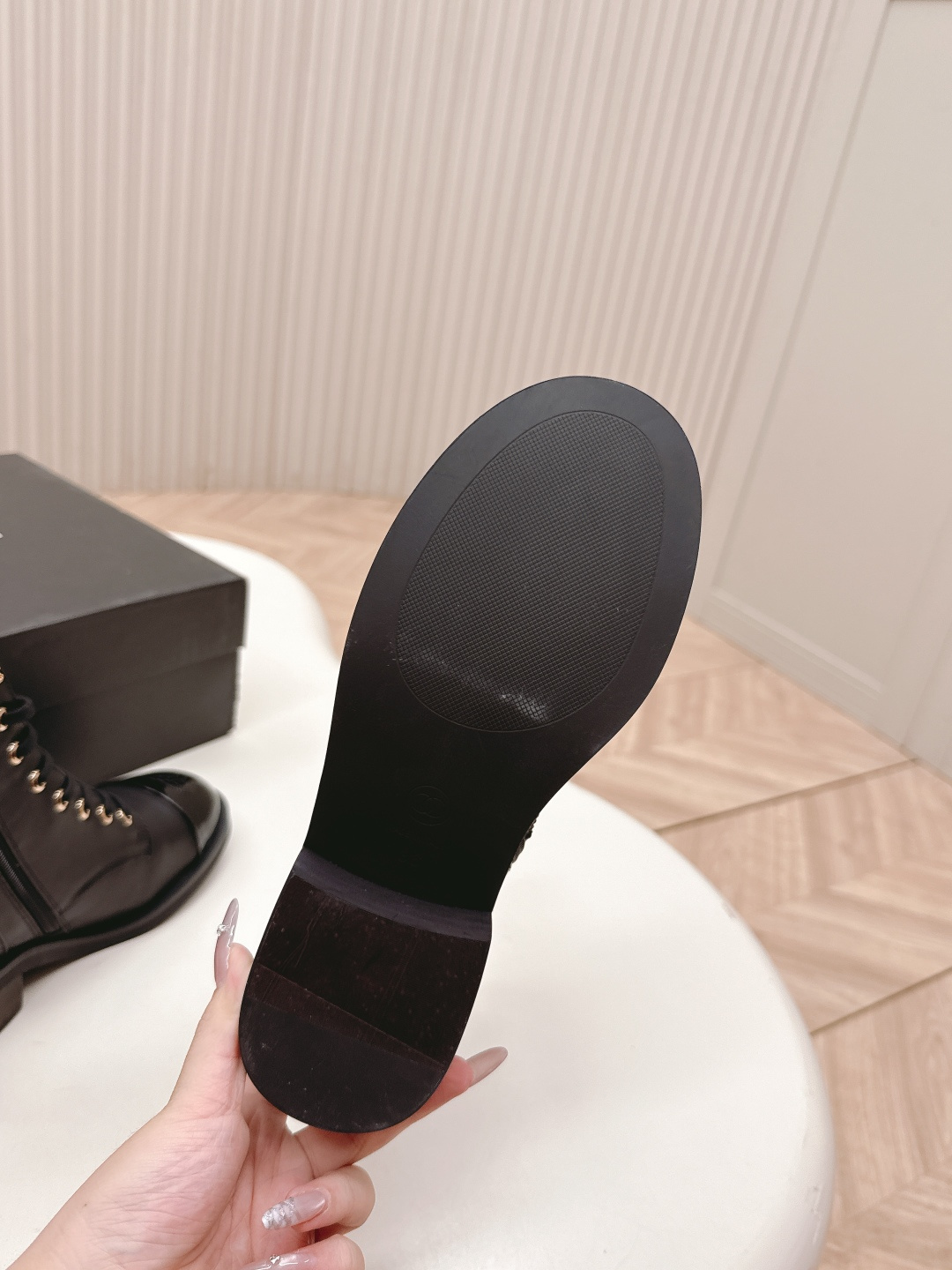 Pair of black leather lace-up combat boots with patent leather toe caps and gold hardware on a white table next to a black shoe box. - Hình 6