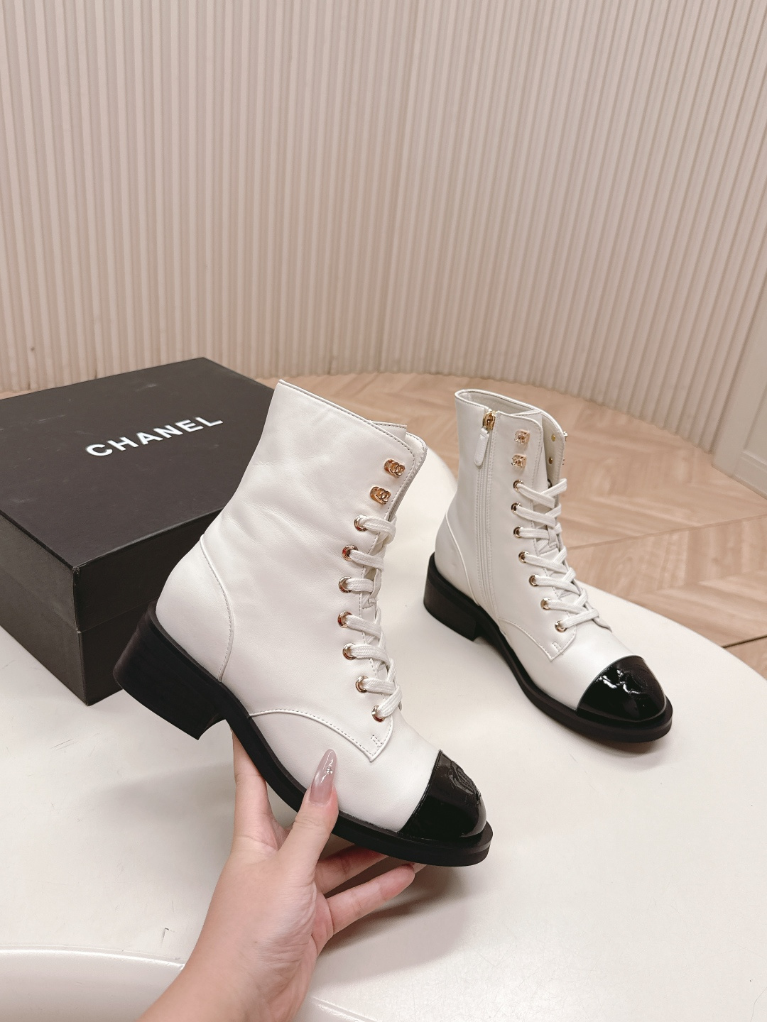 A pair of white leather lace-up combat boots with black patent leather cap toes and gold-tone hardware hooks. - Hình 6