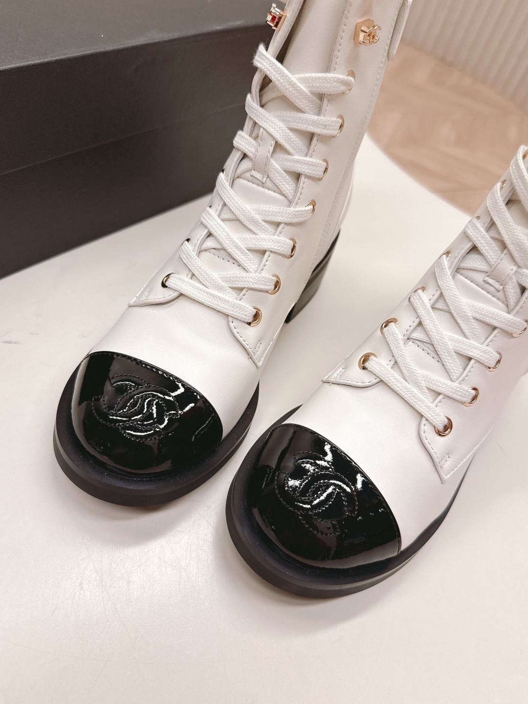 A pair of white leather lace-up combat boots with black patent leather cap toes and gold-tone hardware hooks. - Hình 5