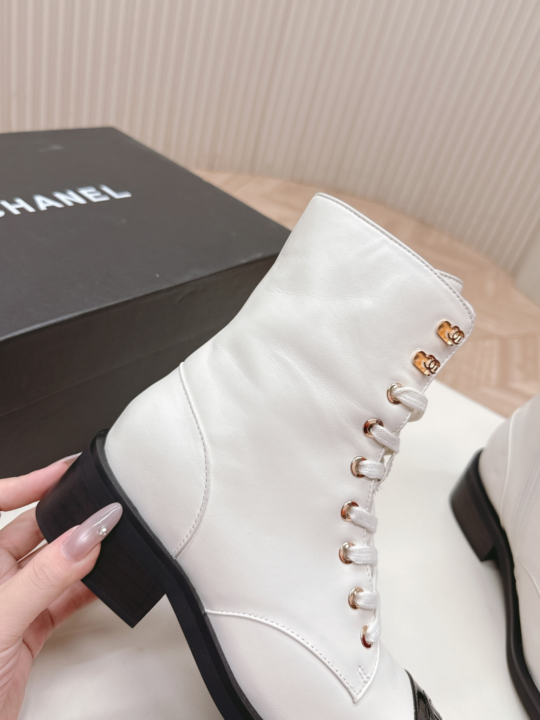 A pair of white leather lace-up combat boots with black patent leather cap toes and gold-tone hardware hooks. - Hình 4