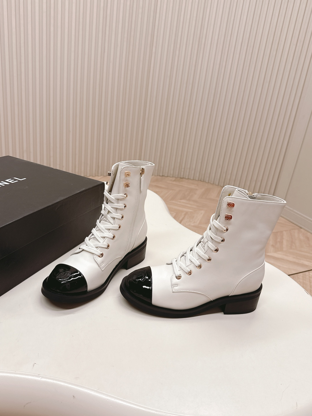 A pair of white leather lace-up combat boots with black patent leather cap toes and gold-tone hardware hooks. - Hình 3
