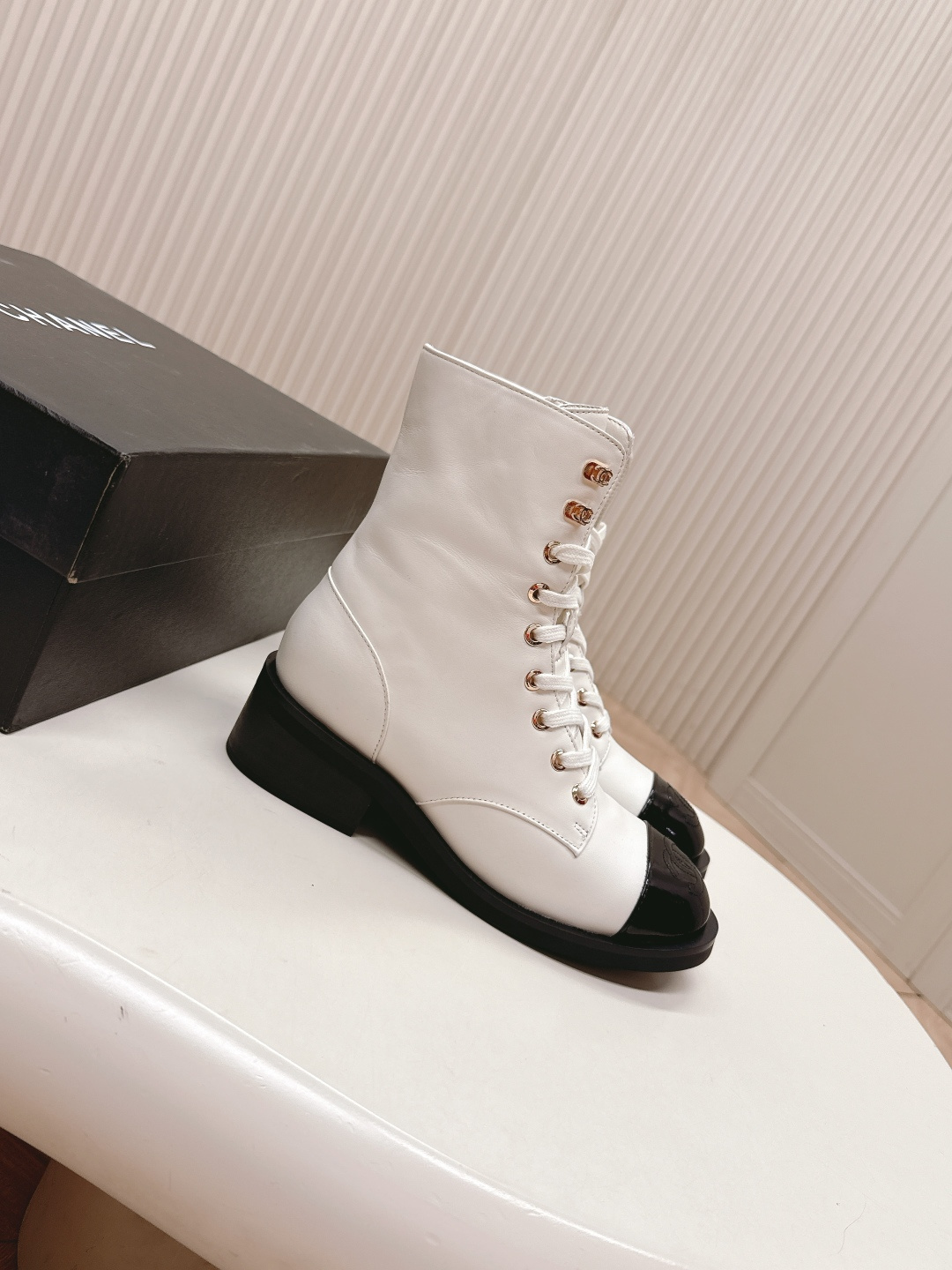 A pair of white leather lace-up combat boots with black patent leather cap toes and gold-tone hardware hooks. - Hình 2