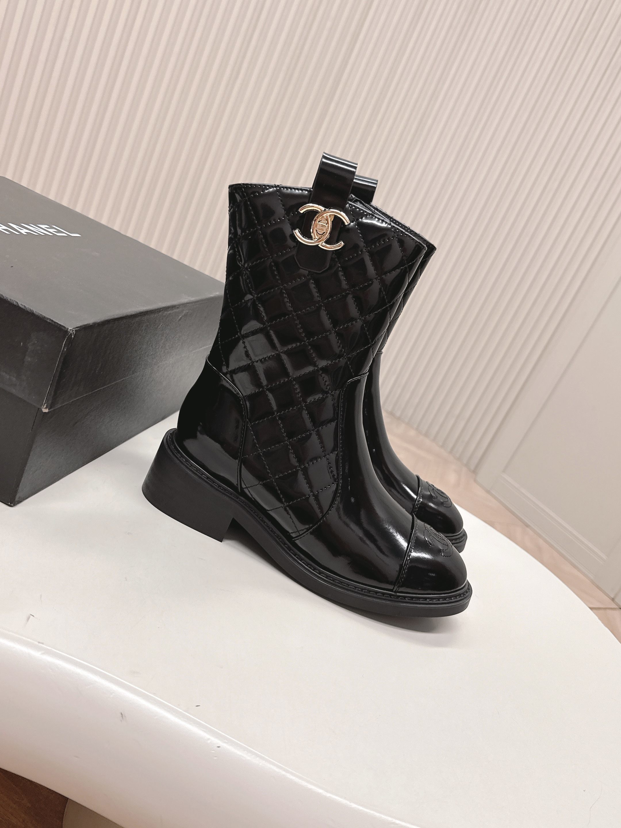 A pair of black Chanel quilted patent leather boots with gold CC logo and side zipper on a white surface. - Hình 6