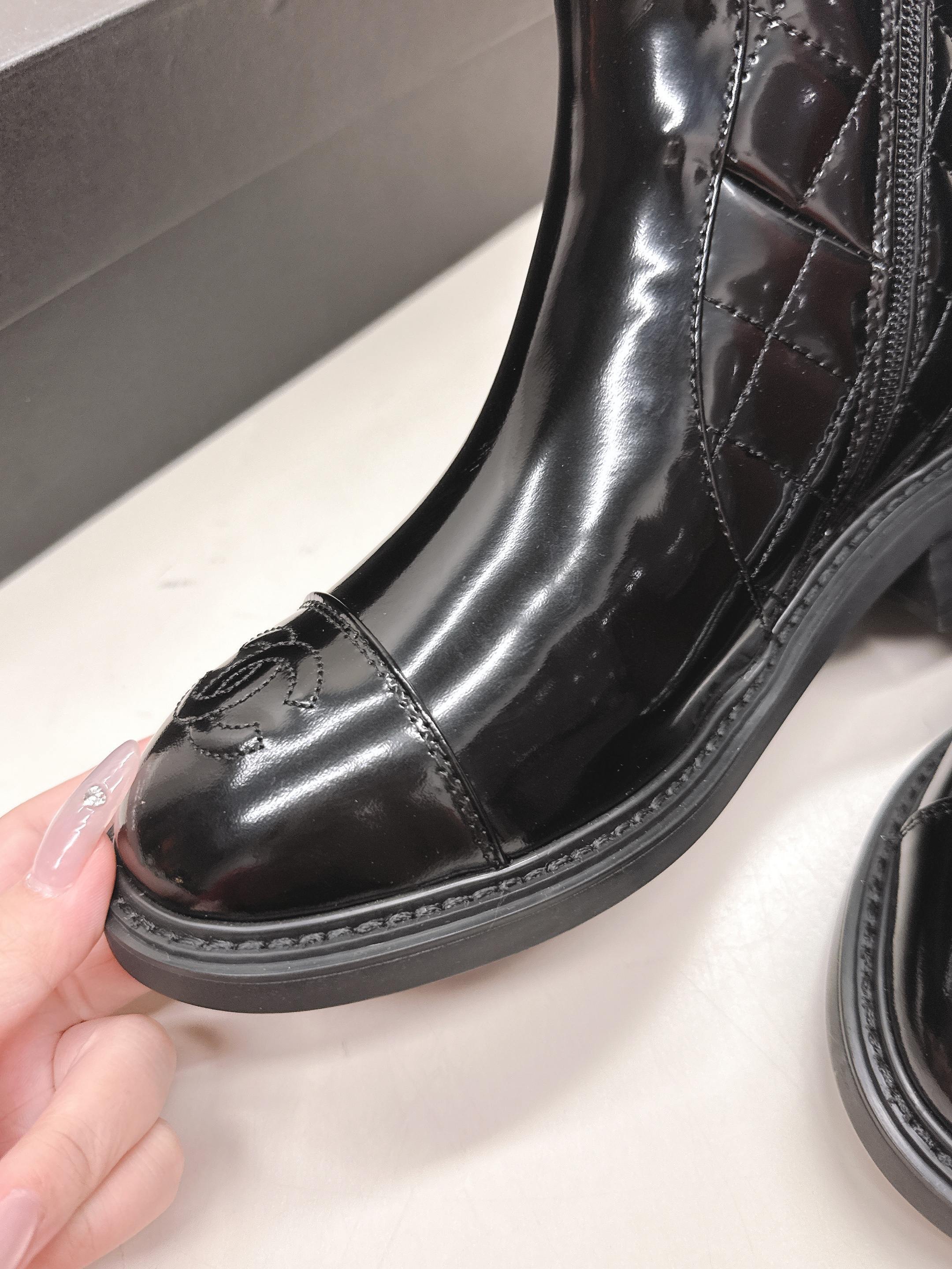 A pair of black Chanel quilted patent leather boots with gold CC logo and side zipper on a white surface. - Hình 4