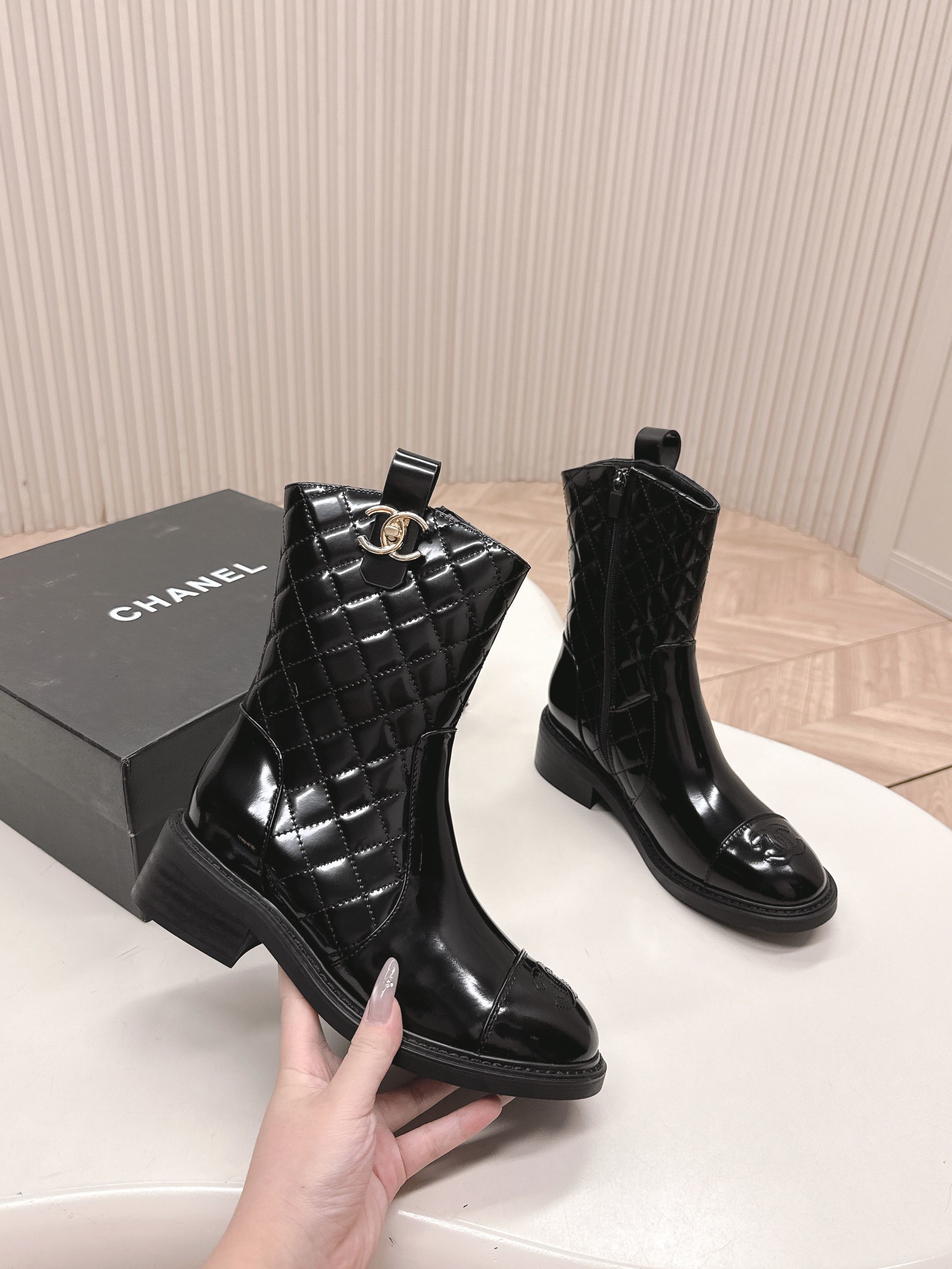 A pair of black Chanel quilted patent leather boots with gold CC logo and side zipper on a white surface. - Hình 2