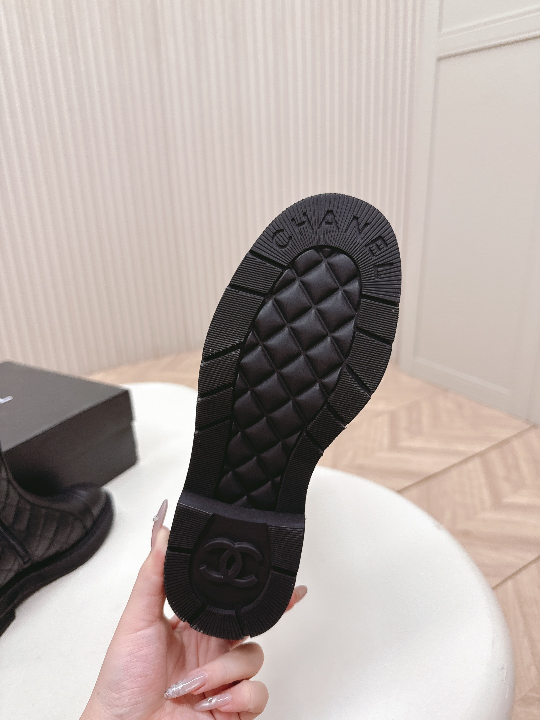 A pair of luxury Chanel black quilted leather knee-high boots with the CC logo on the toe cap and a chunky lug sole, displayed next to a Chanel shoe box. - Hình 5