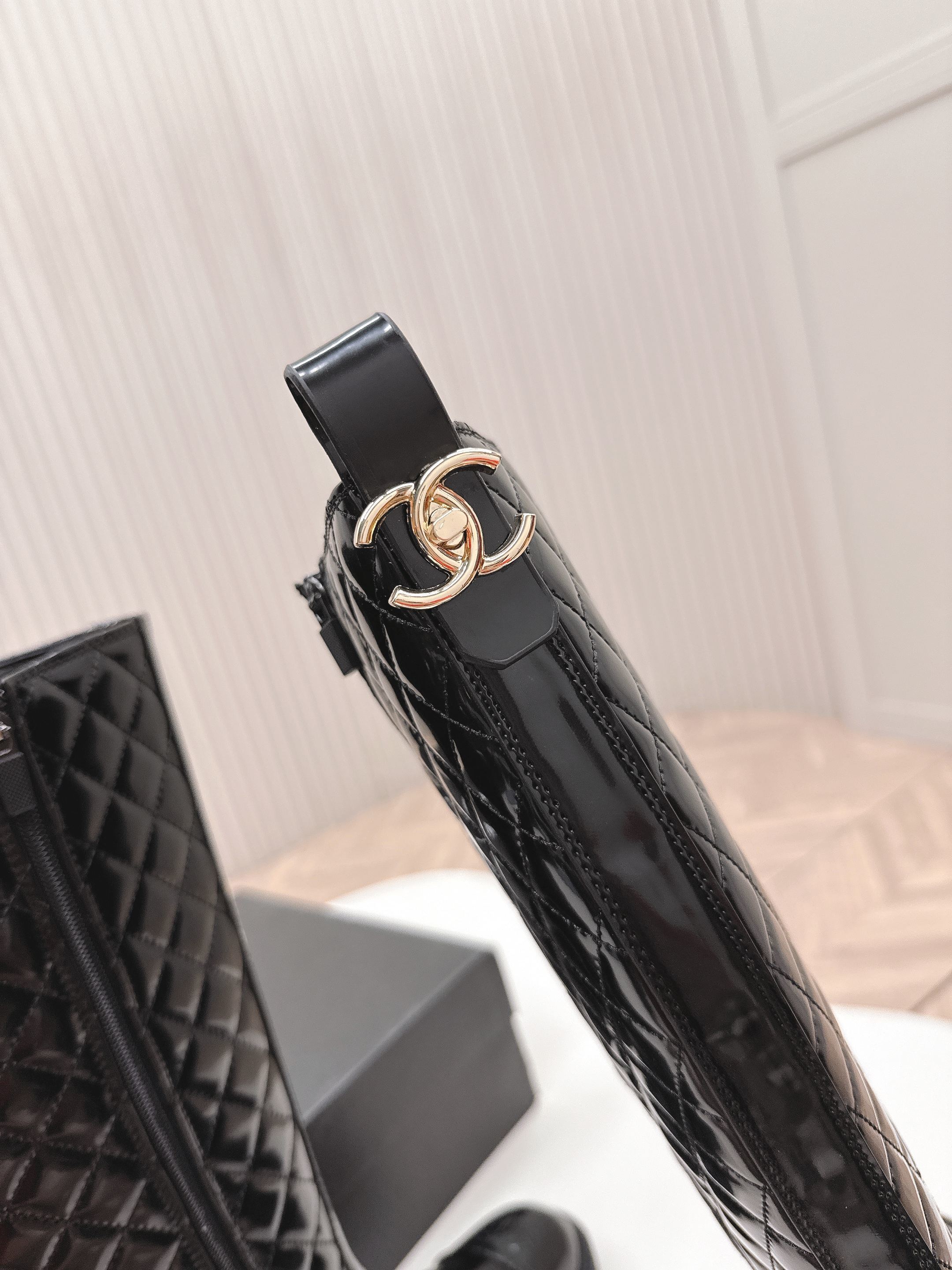 Pair of black Chanel quilted patent leather knee-high boots with CC logo on toe and chunky soles next to a Chanel box - Hình 9