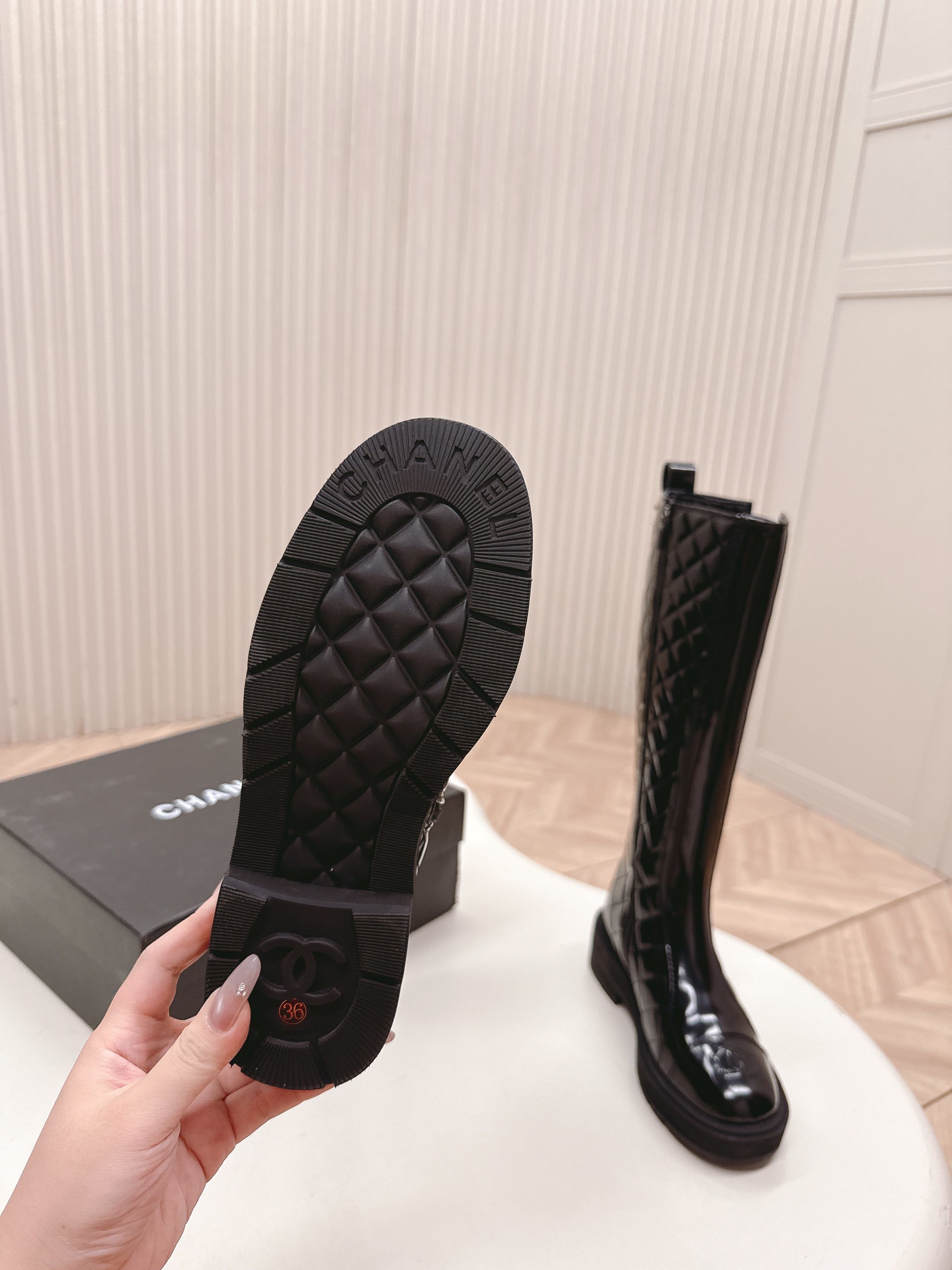 Pair of black Chanel quilted patent leather knee-high boots with CC logo on toe and chunky soles next to a Chanel box - Hình 7
