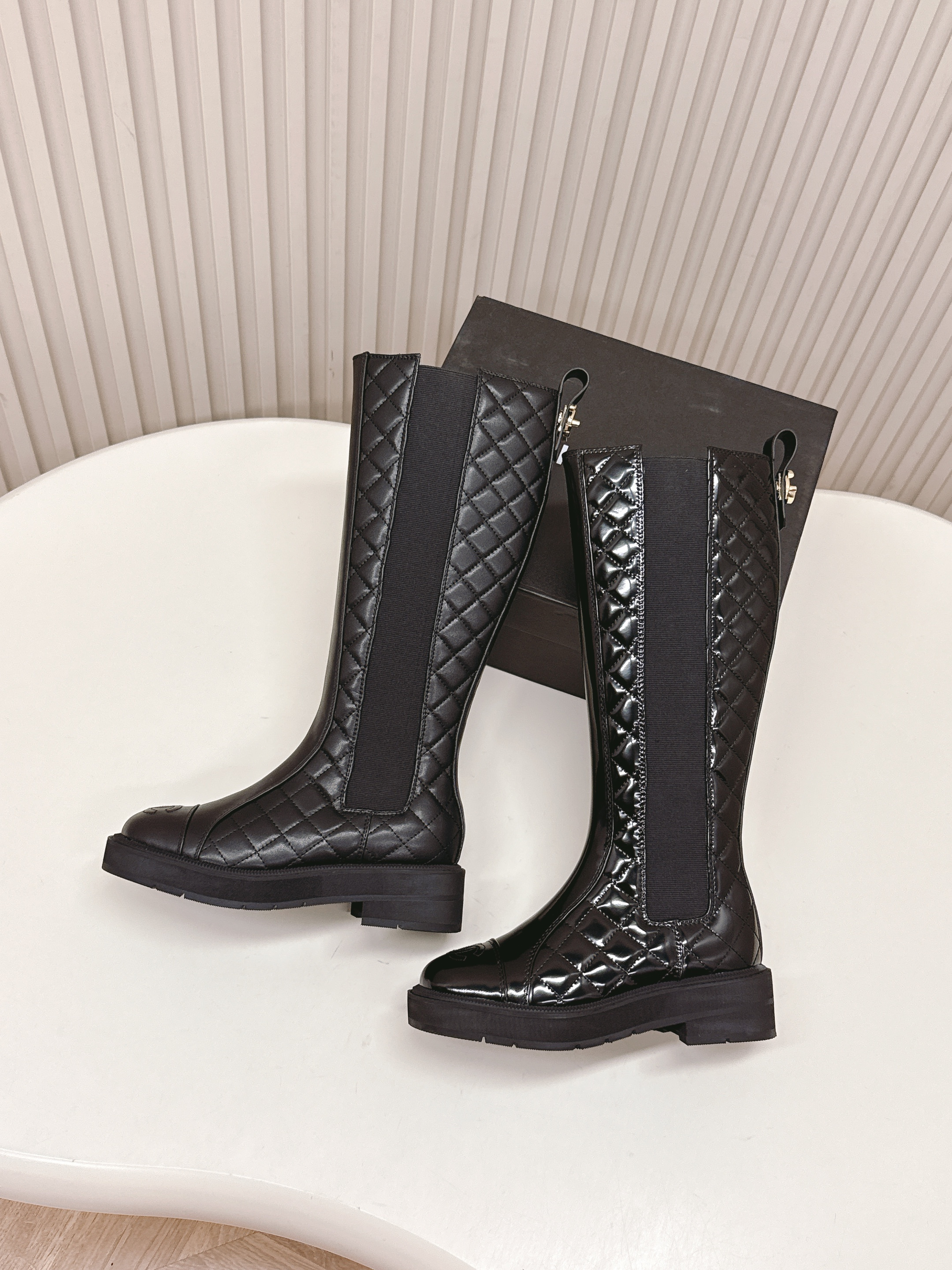 Pair of black Chanel quilted patent leather knee-high boots with CC logo on toe and chunky soles next to a Chanel box - Hình 6