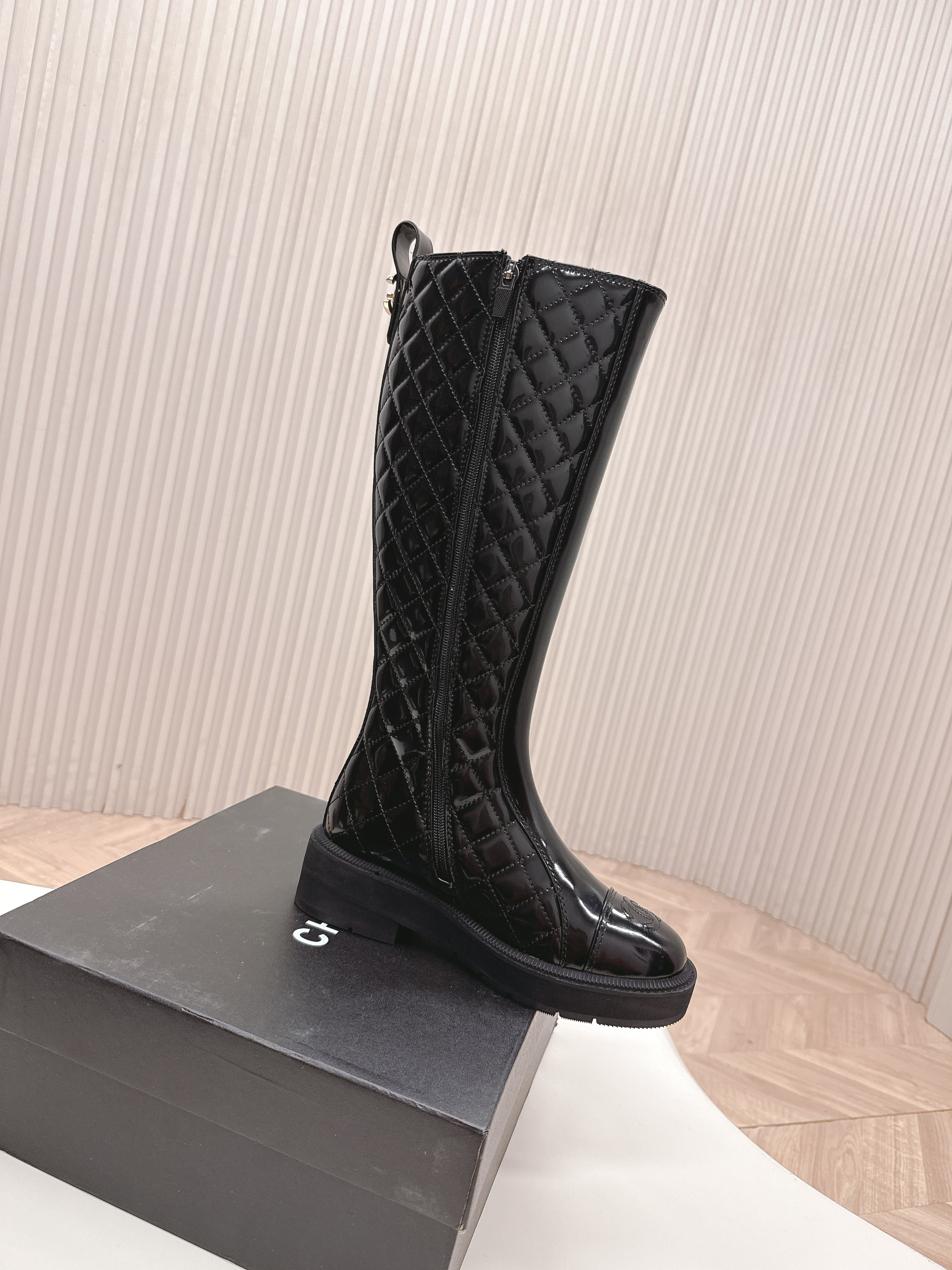 Pair of black Chanel quilted patent leather knee-high boots with CC logo on toe and chunky soles next to a Chanel box - Hình 4