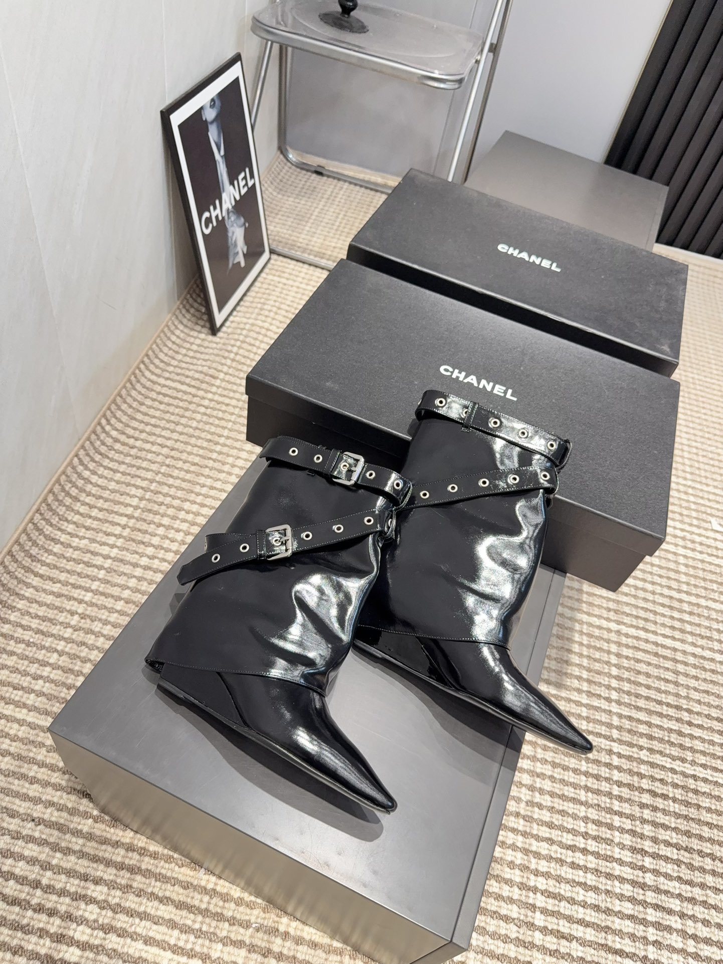 A pair of shiny black Chanel patent leather ankle boots featuring multiple silver buckle straps and a sharp pointed toe sitting on a designer box. - Hình 8