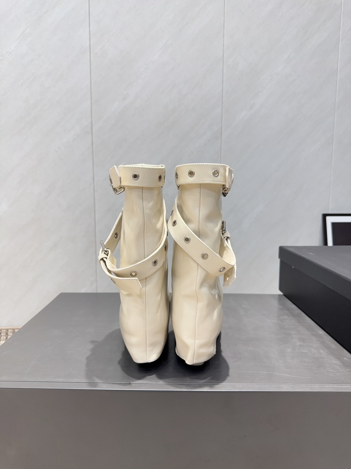 A pair of Chanel cream leather slouchy ankle boots with silver buckle straps and pointed toes placed on a black branded box. - Hình 8