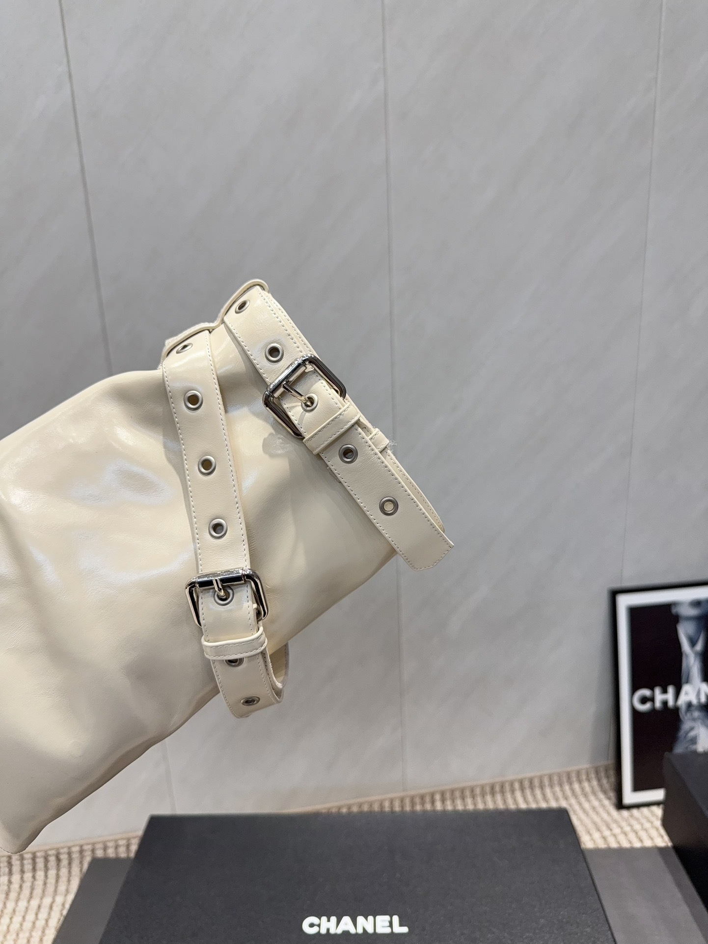 A pair of Chanel cream leather slouchy ankle boots with silver buckle straps and pointed toes placed on a black branded box. - Hình 7