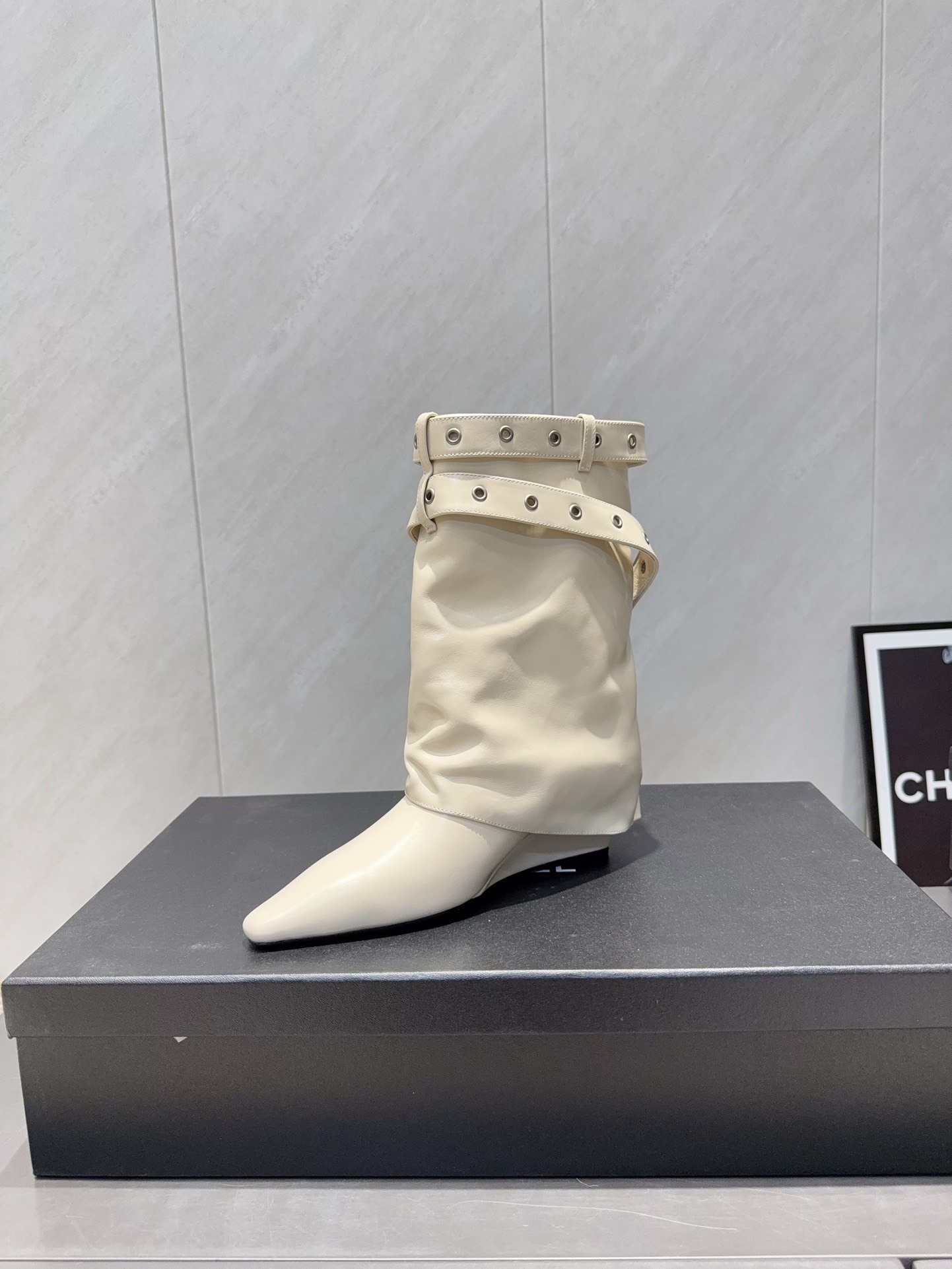 A pair of Chanel cream leather slouchy ankle boots with silver buckle straps and pointed toes placed on a black branded box. - Hình 6