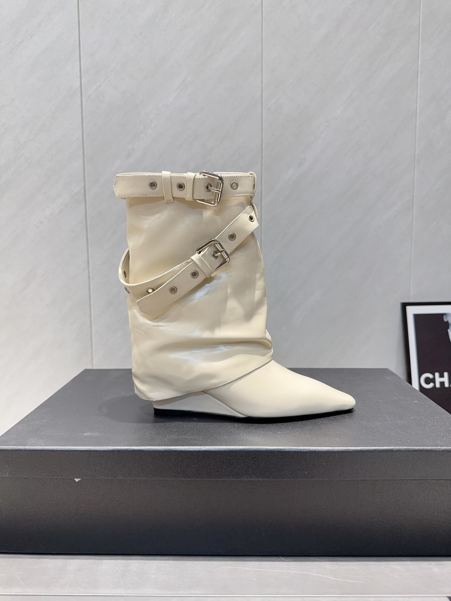 A pair of Chanel cream leather slouchy ankle boots with silver buckle straps and pointed toes placed on a black branded box. - Hình 5