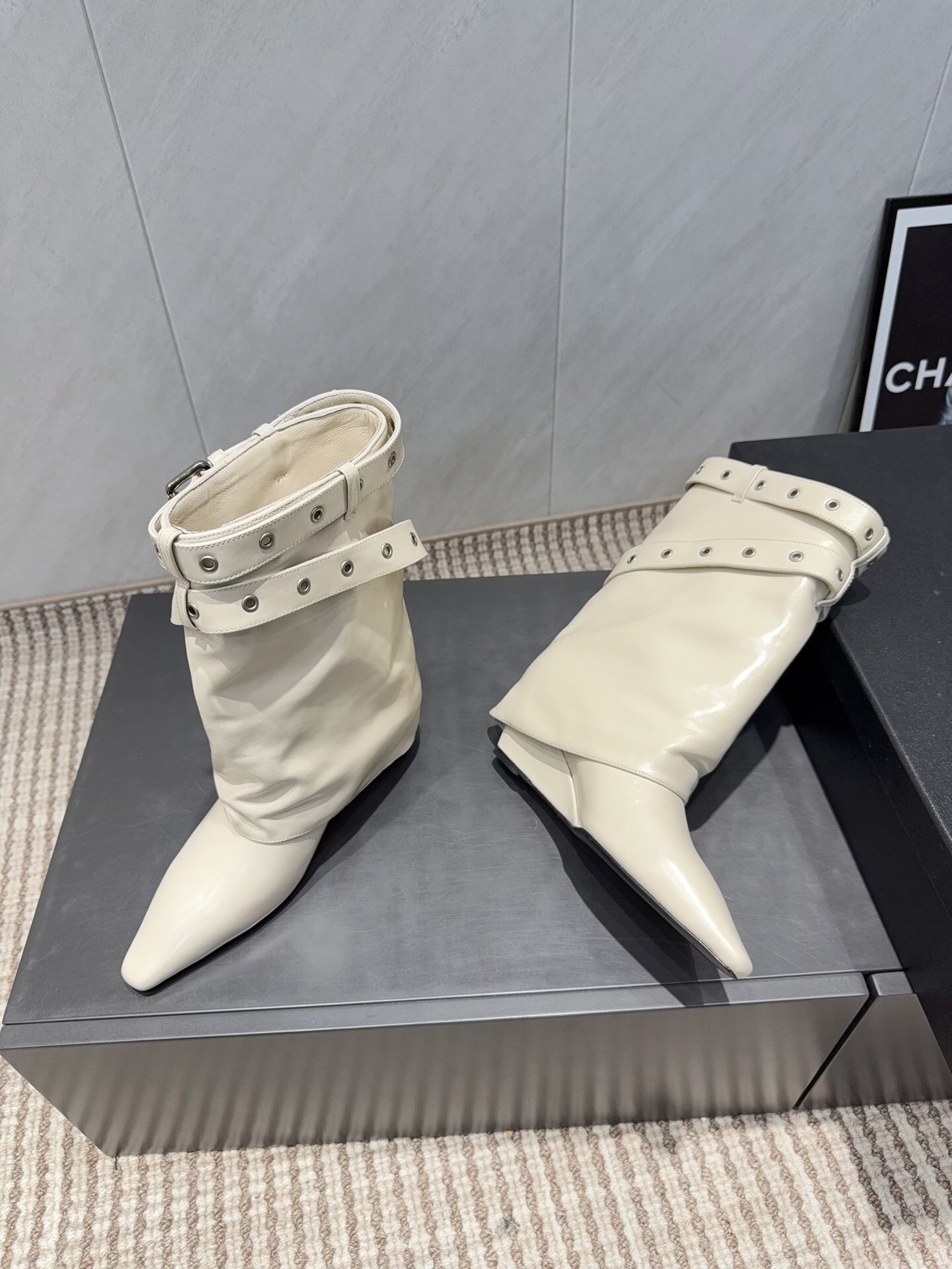 A pair of Chanel cream leather slouchy ankle boots with silver buckle straps and pointed toes placed on a black branded box. - Hình 4