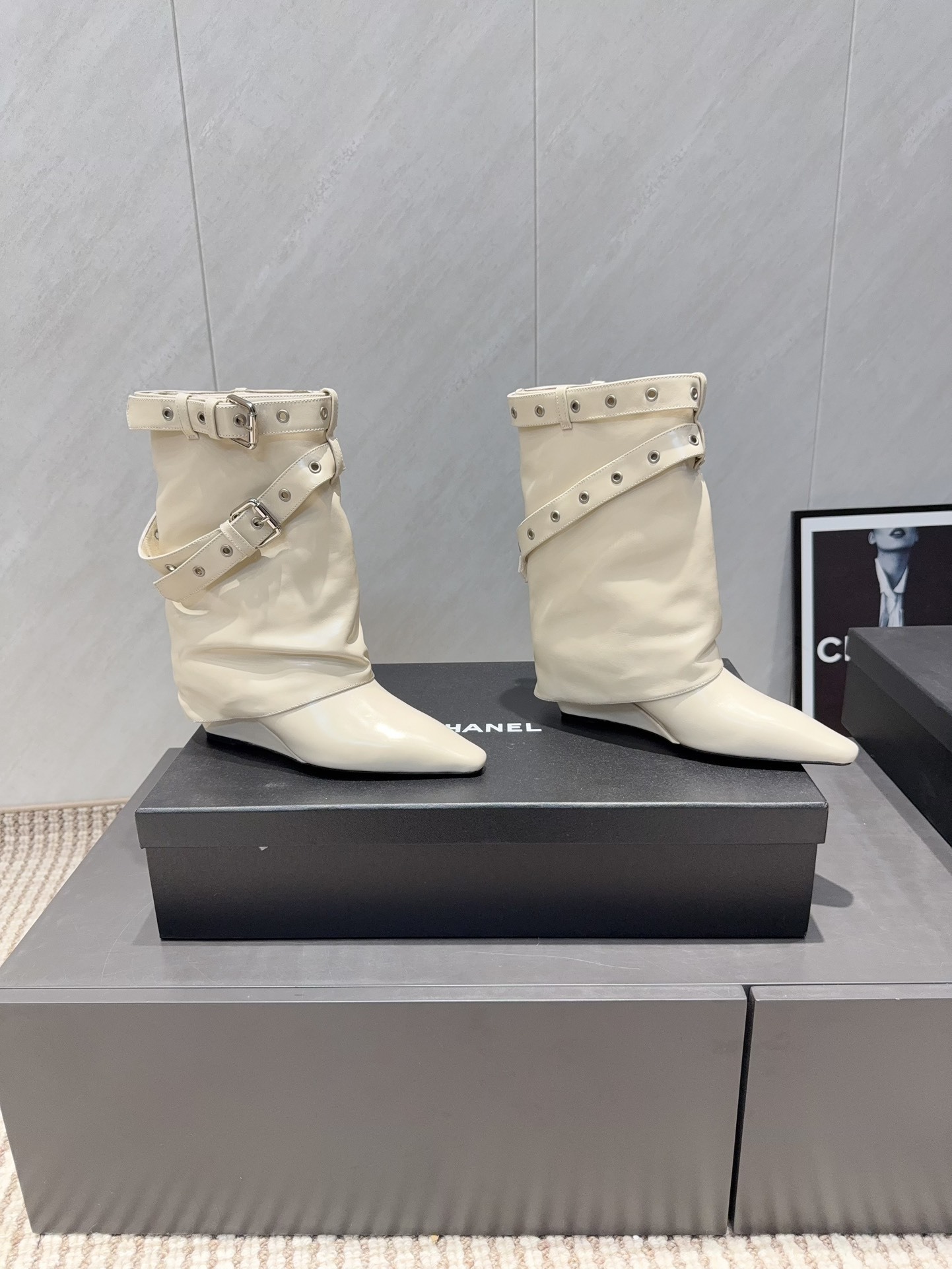 A pair of Chanel cream leather slouchy ankle boots with silver buckle straps and pointed toes placed on a black branded box. - Hình 3