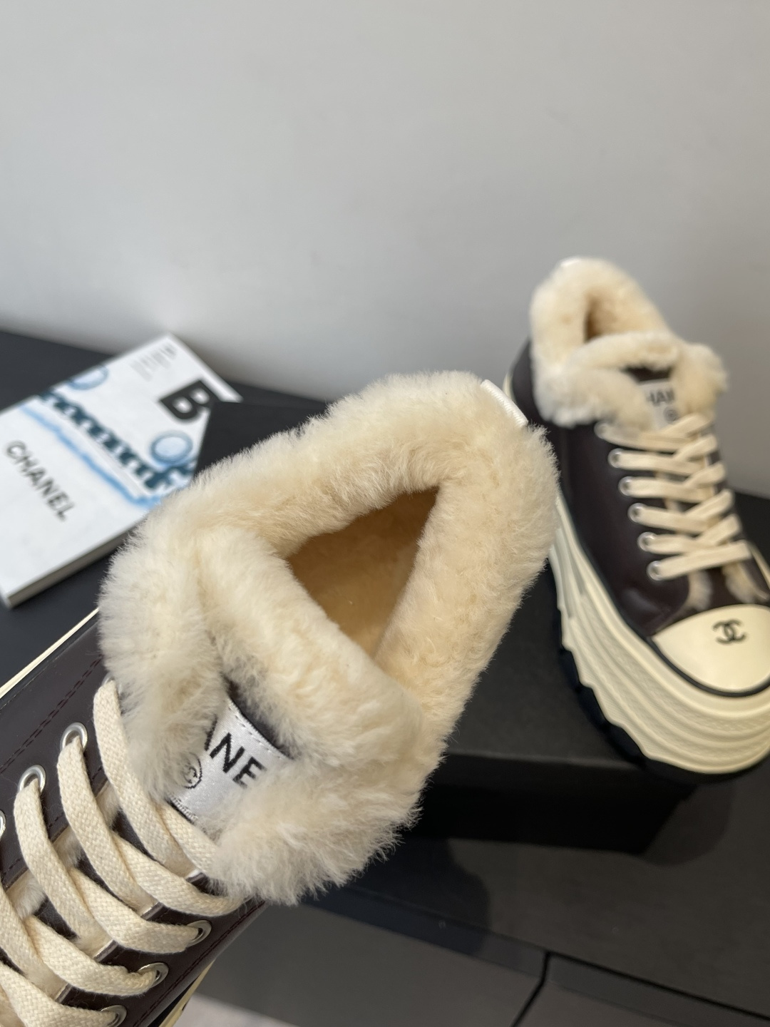 A pair of Chanel brown leather platform sneakers with cream soles and white shearling lining displayed on a black box. - Hình 4