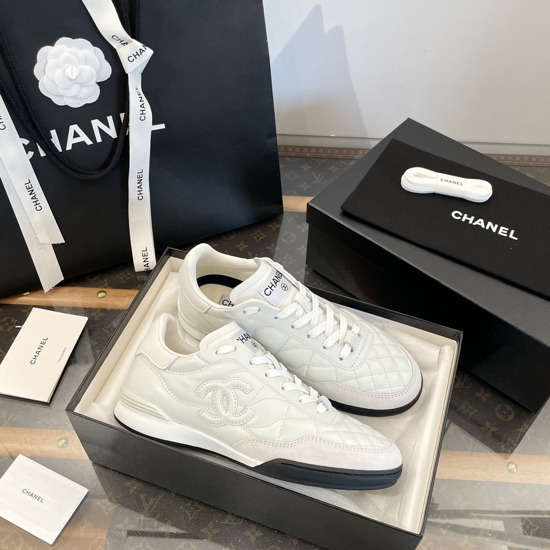 Pair of white Chanel quilted leather sneakers with CC logo, shown with original black packaging and shopping bag. - Hình 7