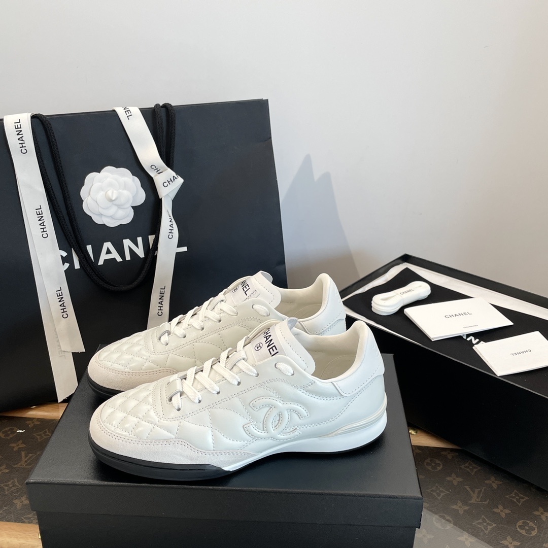 Pair of white Chanel quilted leather sneakers with CC logo, shown with original black packaging and shopping bag. - Hình 6