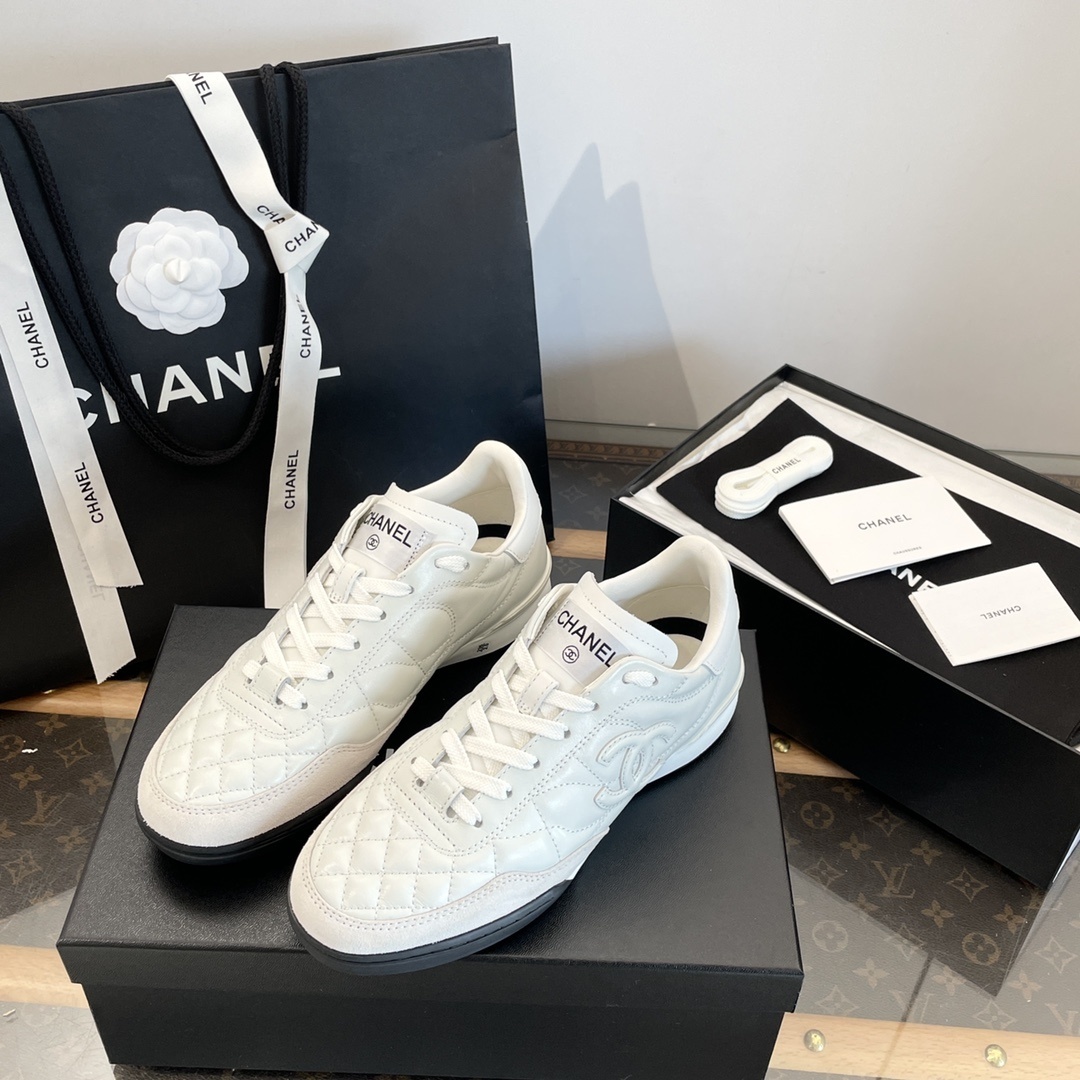 Pair of white Chanel quilted leather sneakers with CC logo, shown with original black packaging and shopping bag. - Hình 3