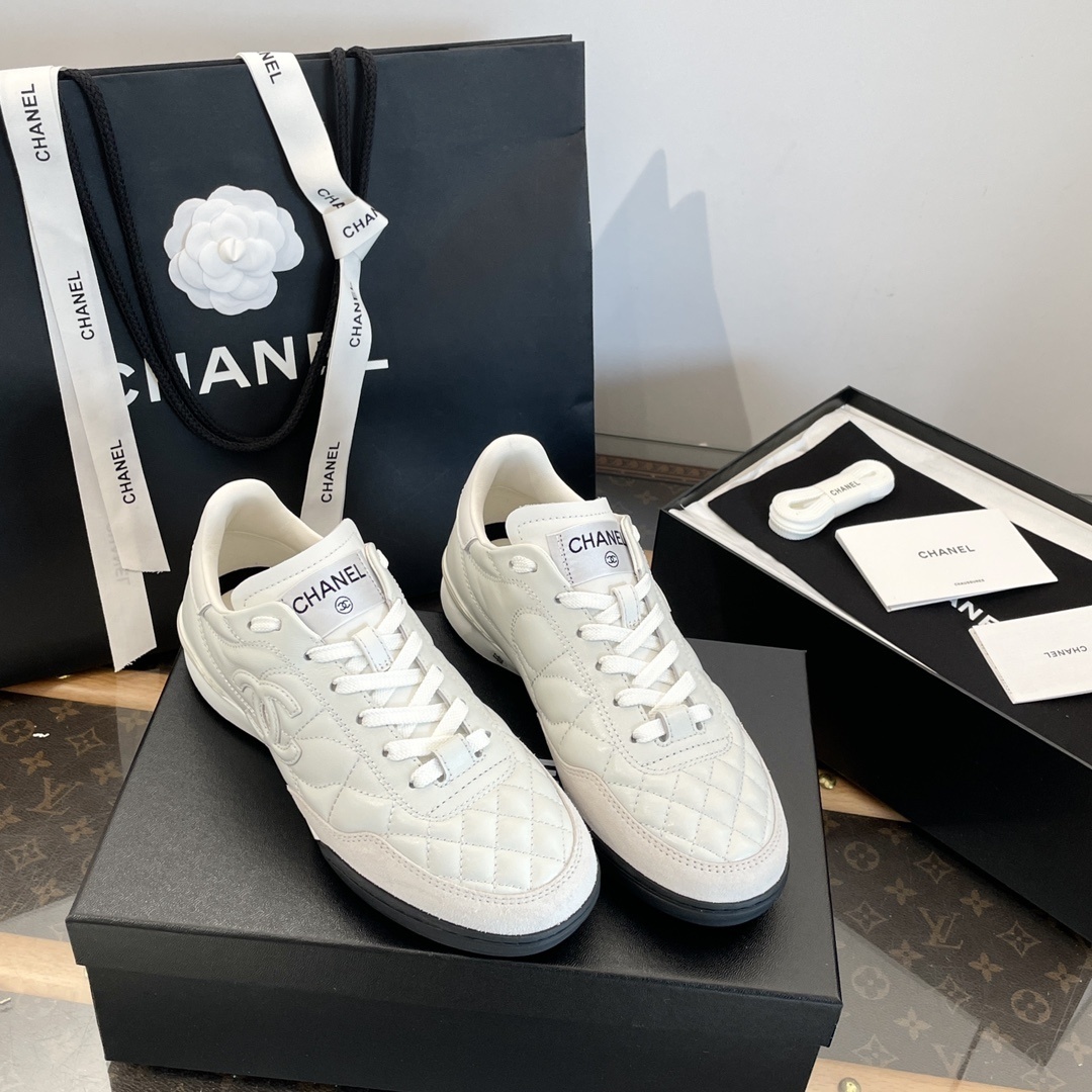 Pair of white Chanel quilted leather sneakers with CC logo, shown with original black packaging and shopping bag. - Hình 2