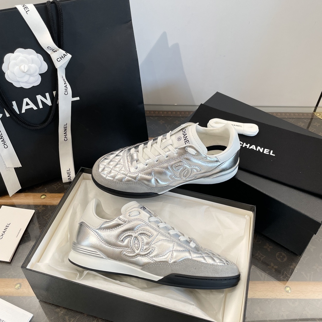 Pair of Chanel metallic silver quilted leather sneakers with CC logo displayed on a black box with shopping bag and accessories. - Hình 8