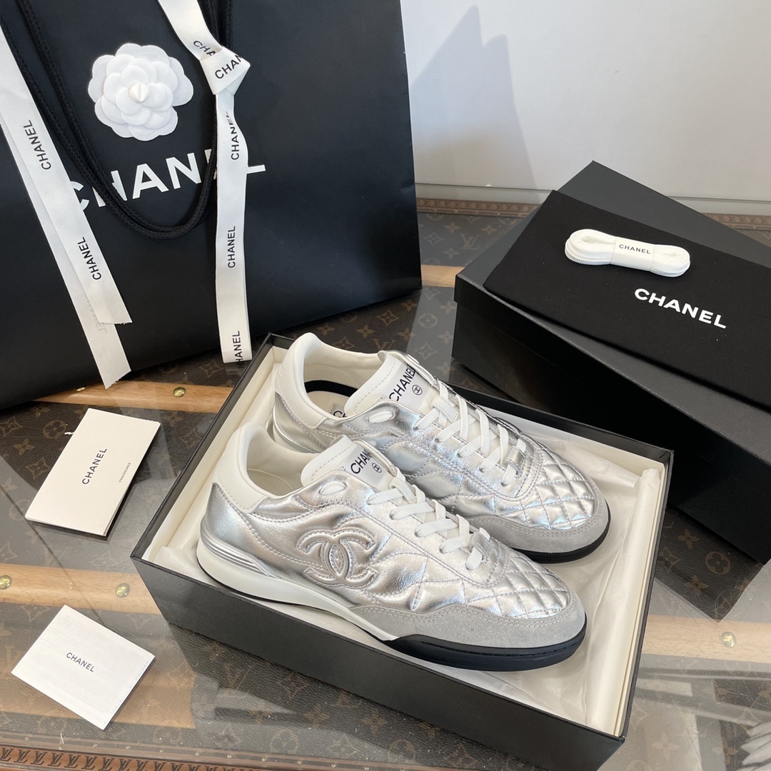 Pair of Chanel metallic silver quilted leather sneakers with CC logo displayed on a black box with shopping bag and accessories. - Hình 7