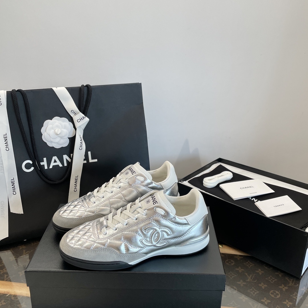 Pair of Chanel metallic silver quilted leather sneakers with CC logo displayed on a black box with shopping bag and accessories. - Hình 6