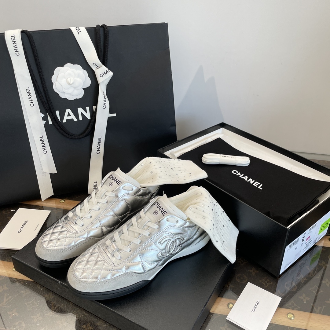 Pair of Chanel metallic silver quilted leather sneakers with CC logo displayed on a black box with shopping bag and accessories. - Hình 5
