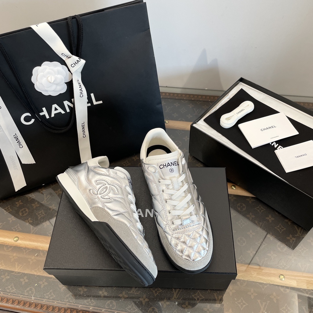 Pair of Chanel metallic silver quilted leather sneakers with CC logo displayed on a black box with shopping bag and accessories. - Hình 4