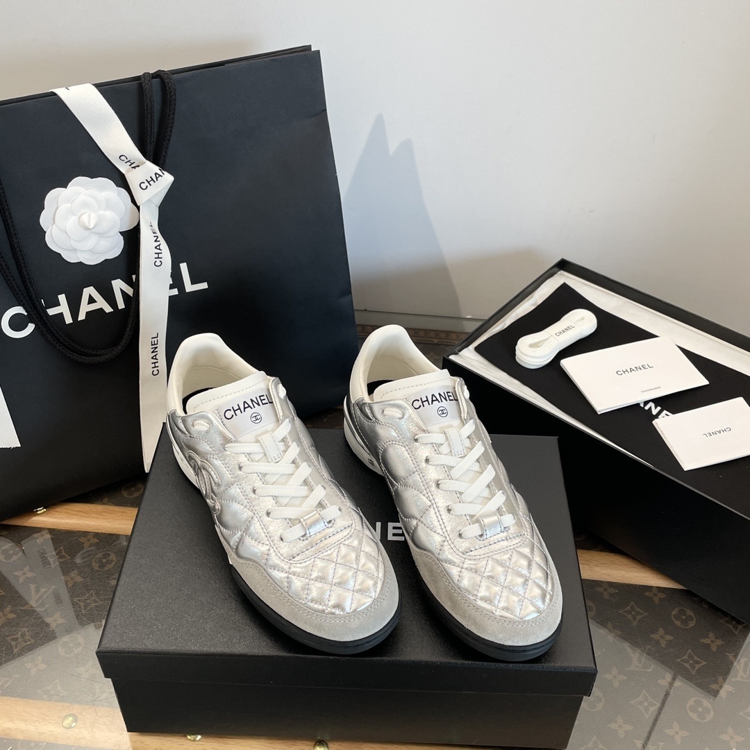 Pair of Chanel metallic silver quilted leather sneakers with CC logo displayed on a black box with shopping bag and accessories. - Hình 2