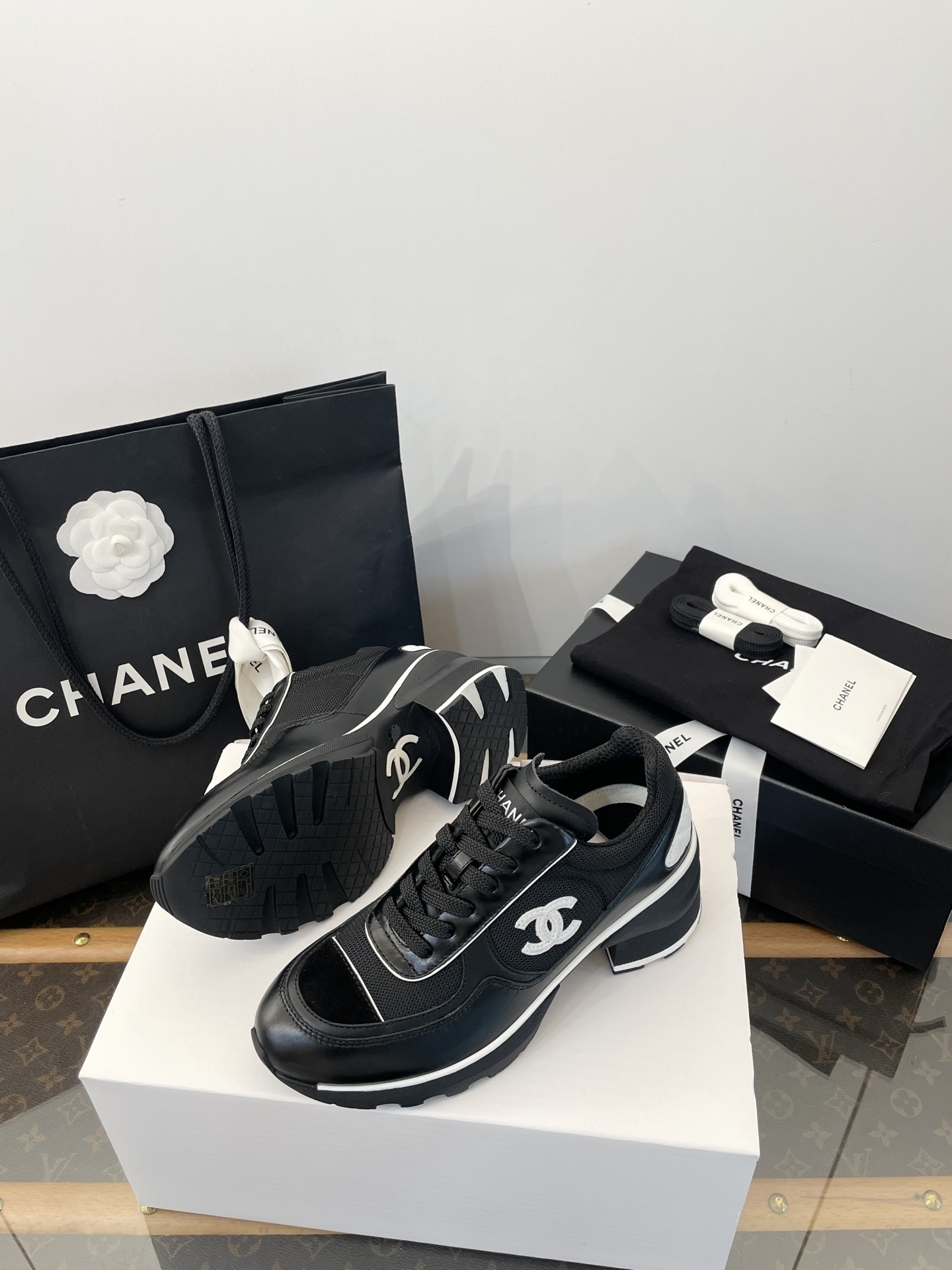 A pair of black Chanel sneakers with white CC logo on a white box with luxury Chanel packaging in the background. - Hình 9