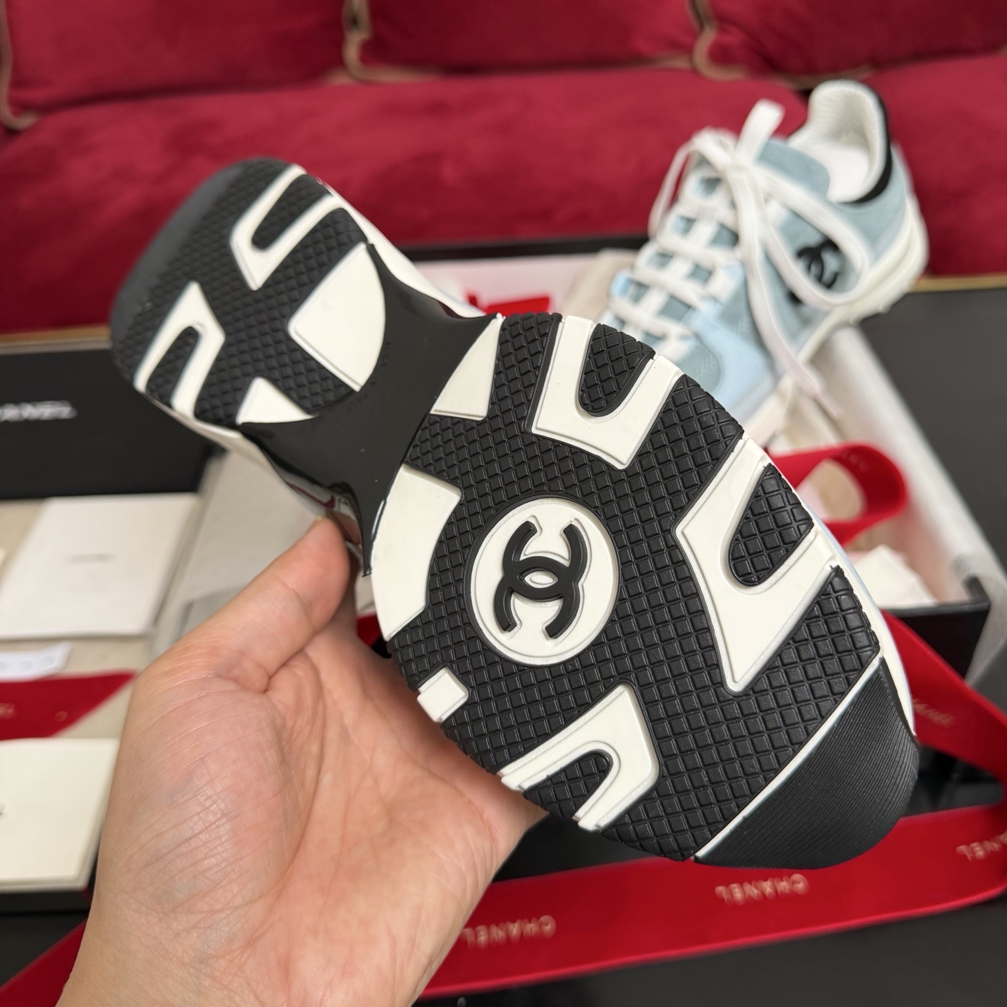 A pair of light blue Chanel sneakers with a black CC logo and white laces displayed with luxury packaging and red ribbons. - Hình 9