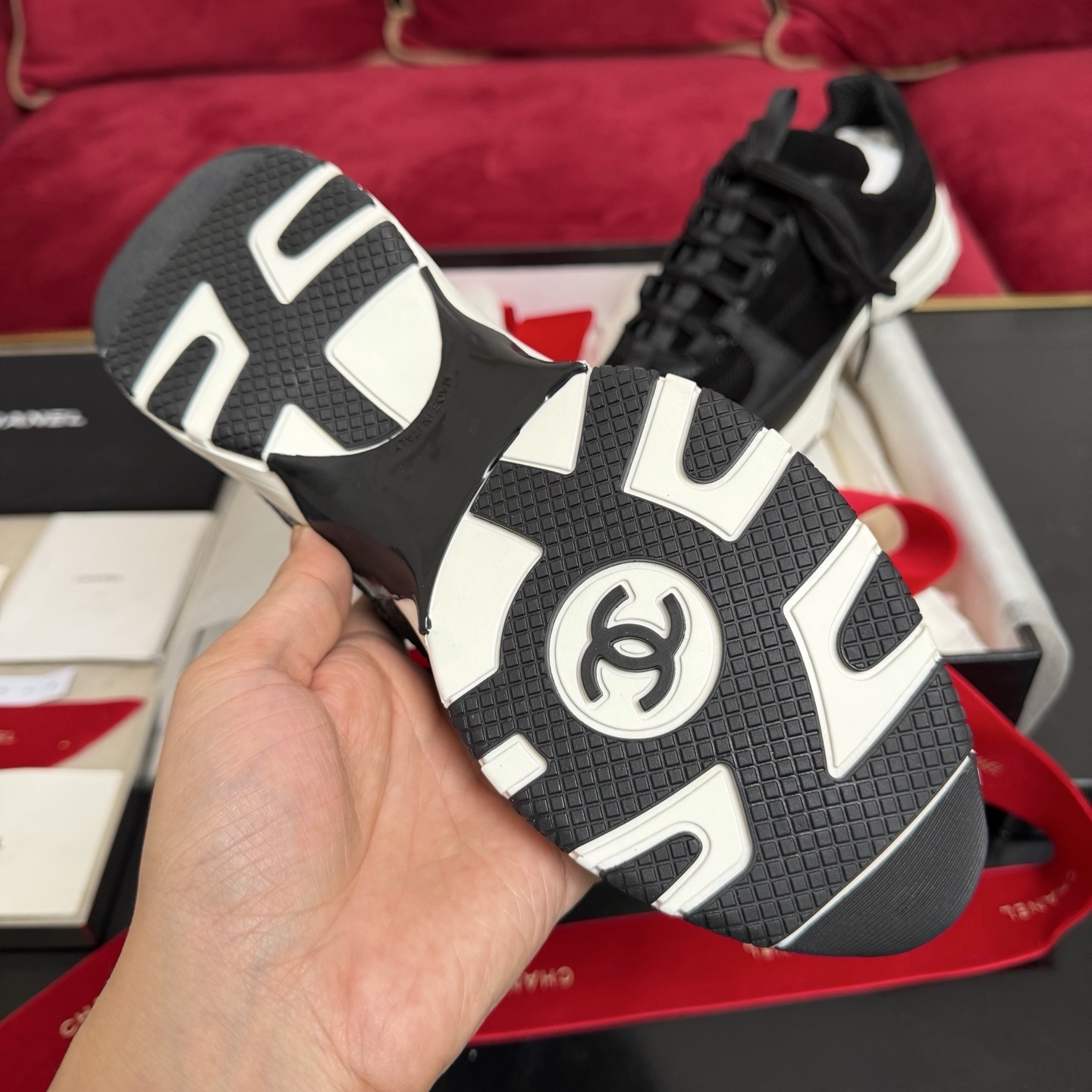 A pair of black Chanel suede and fabric sneakers sitting on a designer box with red ribbons. - Hình 9