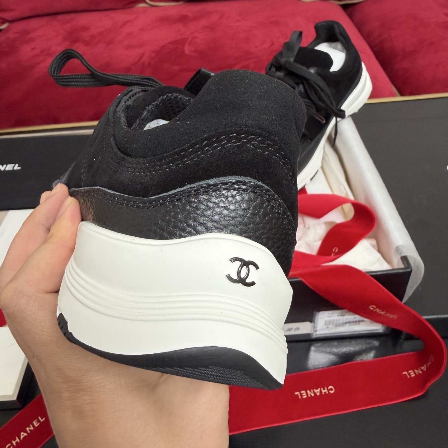 A pair of black Chanel suede and fabric sneakers sitting on a designer box with red ribbons. - Hình 8