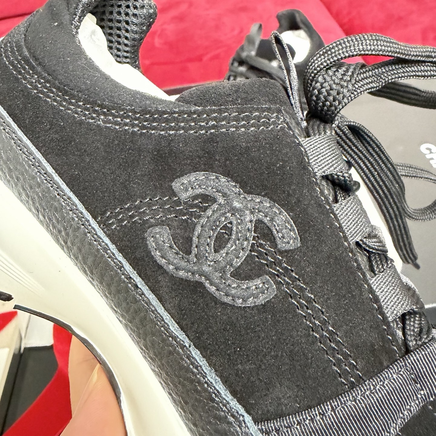 A pair of black Chanel suede and fabric sneakers sitting on a designer box with red ribbons. - Hình 7