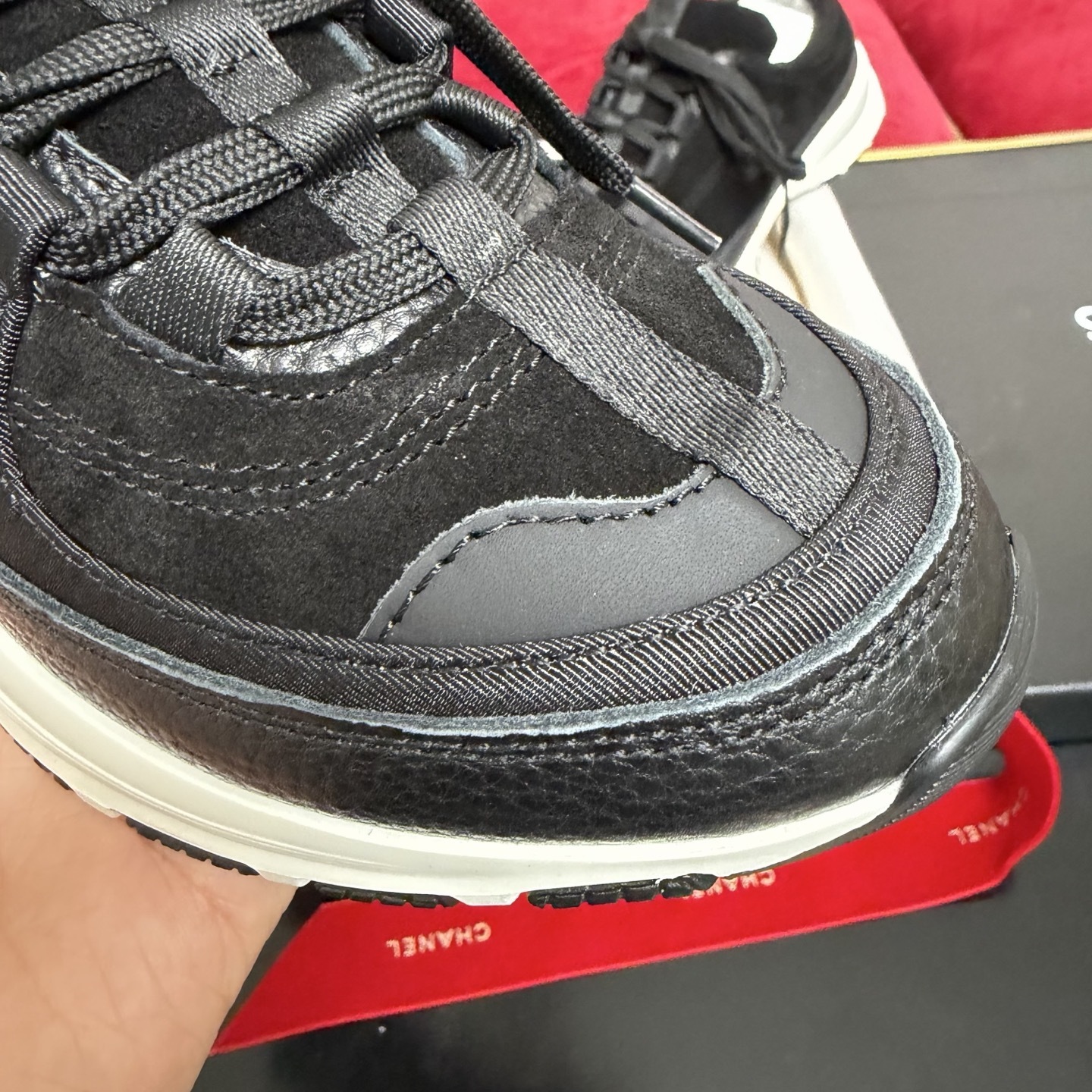 A pair of black Chanel suede and fabric sneakers sitting on a designer box with red ribbons. - Hình 6