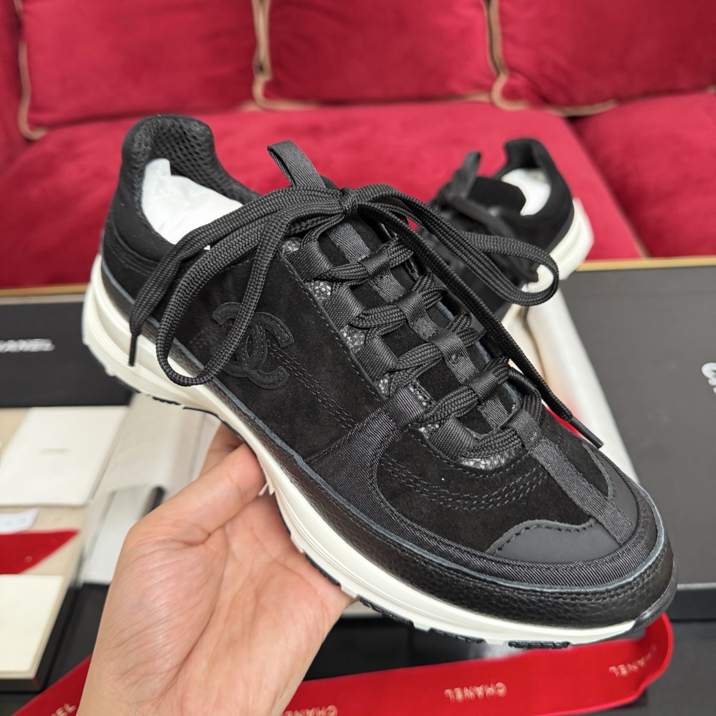 A pair of black Chanel suede and fabric sneakers sitting on a designer box with red ribbons. - Hình 4
