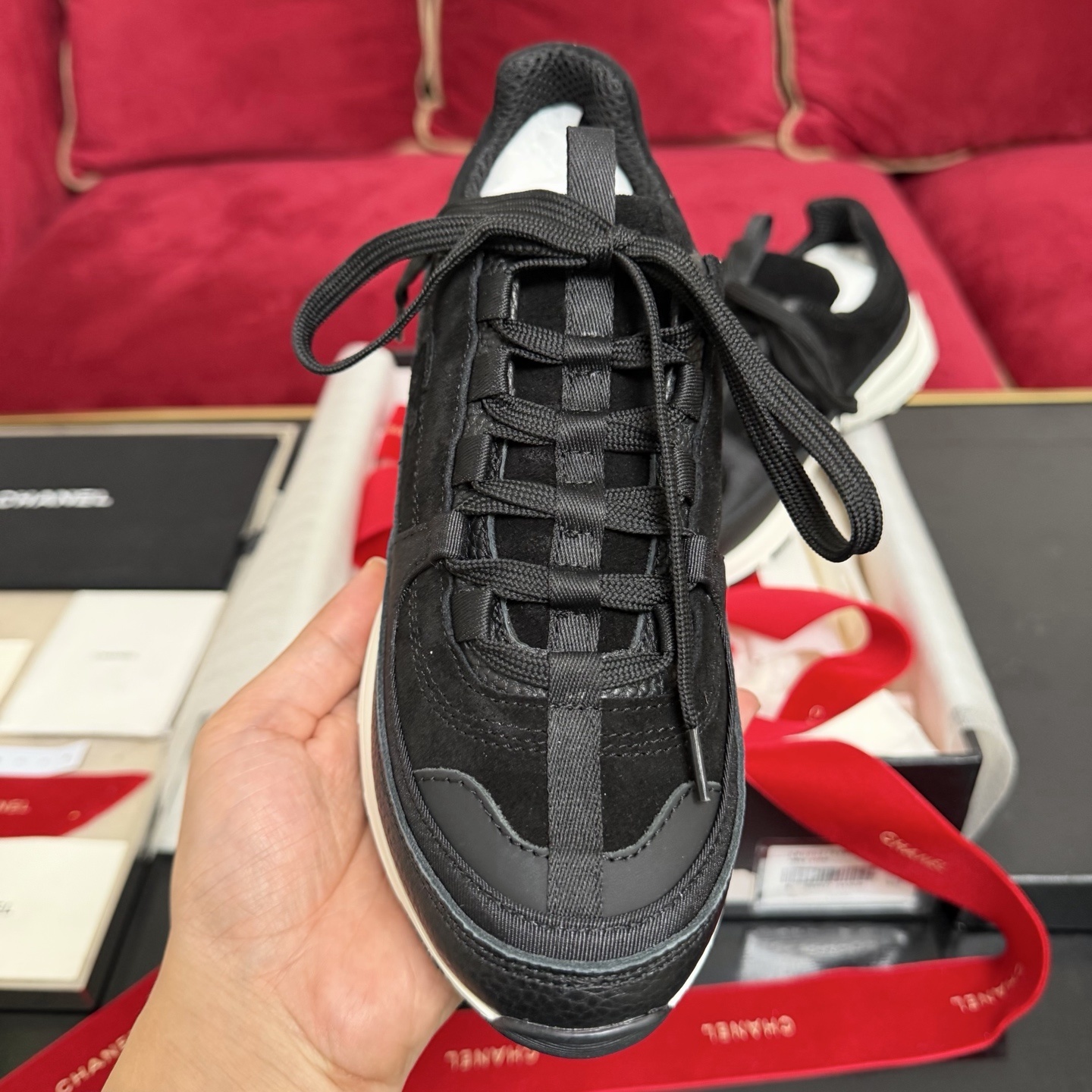 A pair of black Chanel suede and fabric sneakers sitting on a designer box with red ribbons. - Hình 3
