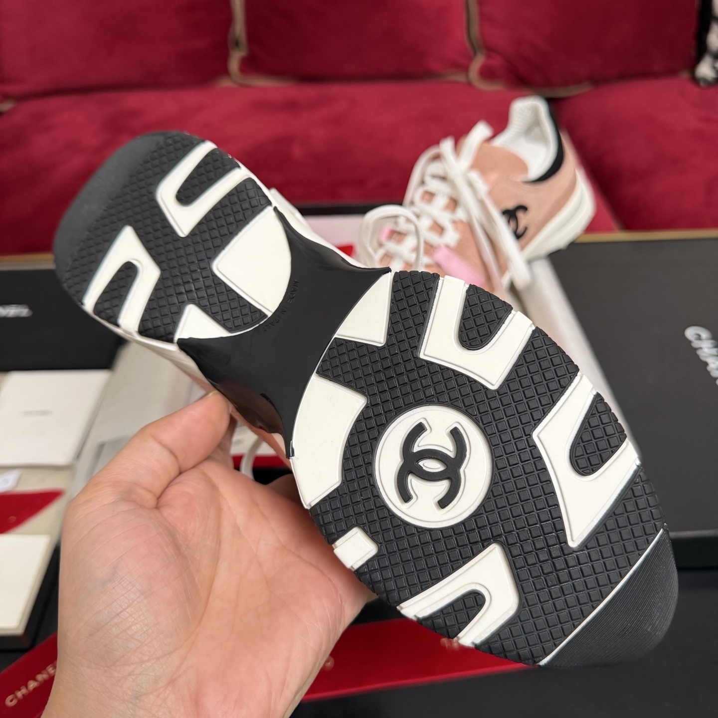 A pair of pink and black Chanel sneakers with white laces sitting on a luxury gift box with red ribbons - Hình 9